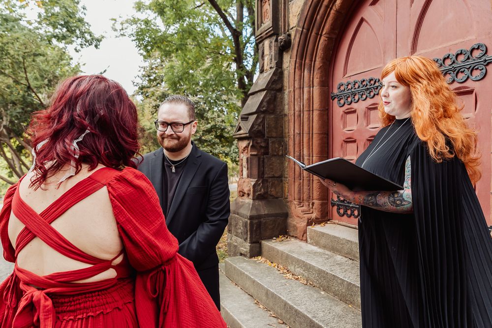 A wedding ceremony on church steps with an officiant in black performing the service.