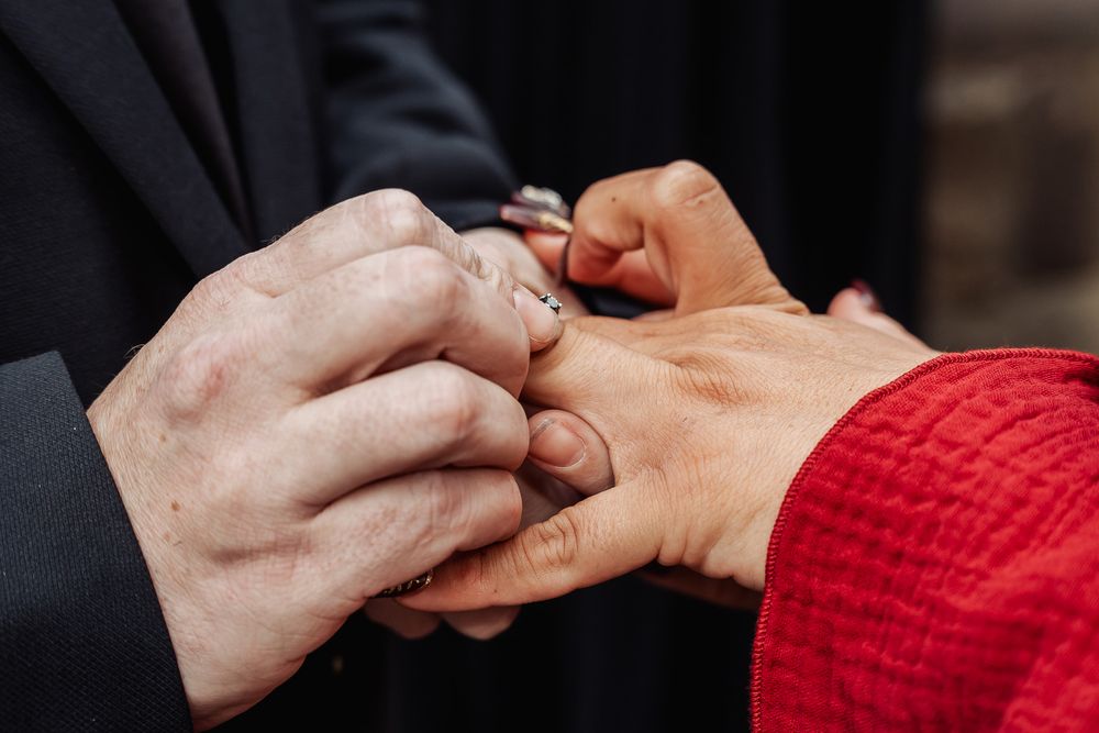 Intimate moment of wedding ring exchange with hands clasped together.