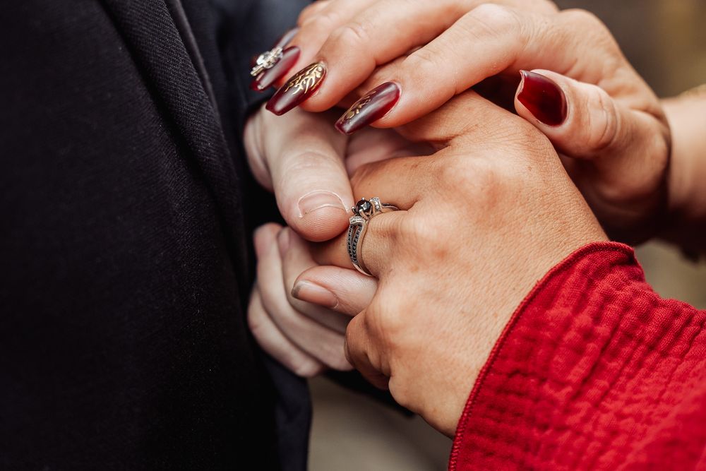 Close-up of hands during a ring exchange ceremony with red and black attire.