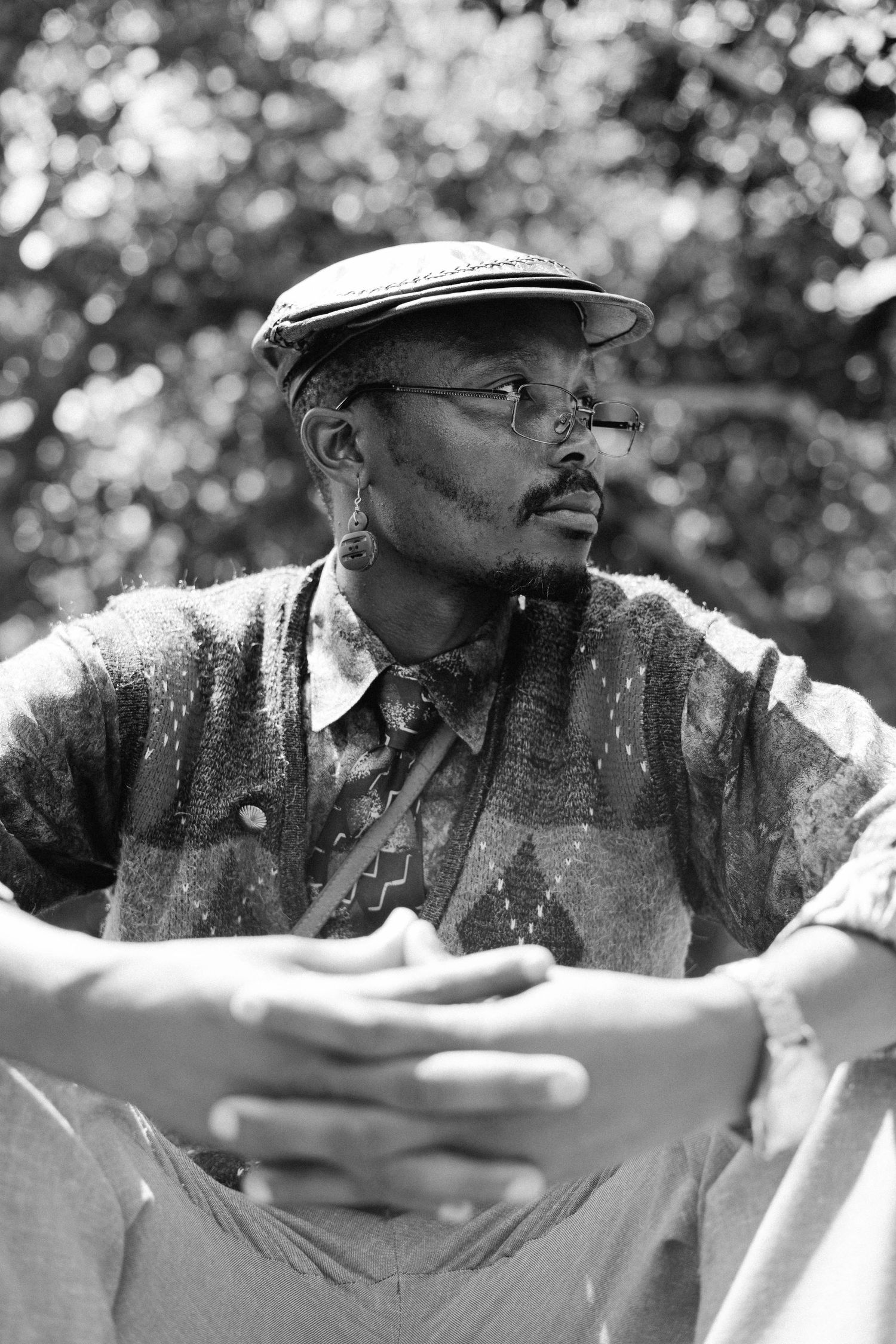 Black and white portrait of a person wearing a flat cap and glasses gazing thoughtfully to the side outdoors.