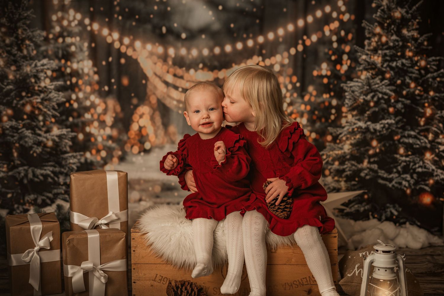 Cozy Christmas scene with siblings in matching red sweaters sitting on a white fur bench among presents.