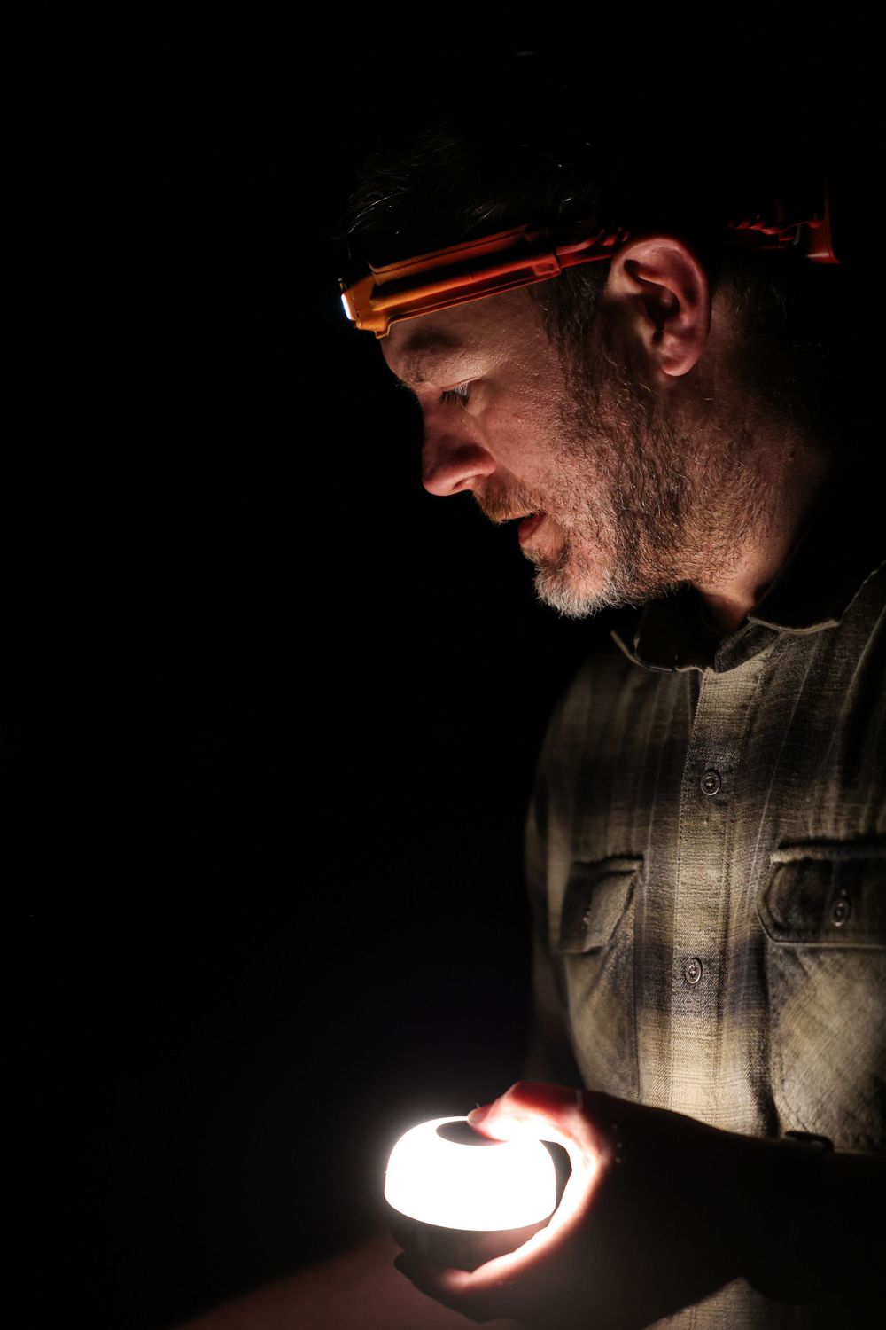 A glowing portable light illuminates someone wearing a headlamp in the darkness.