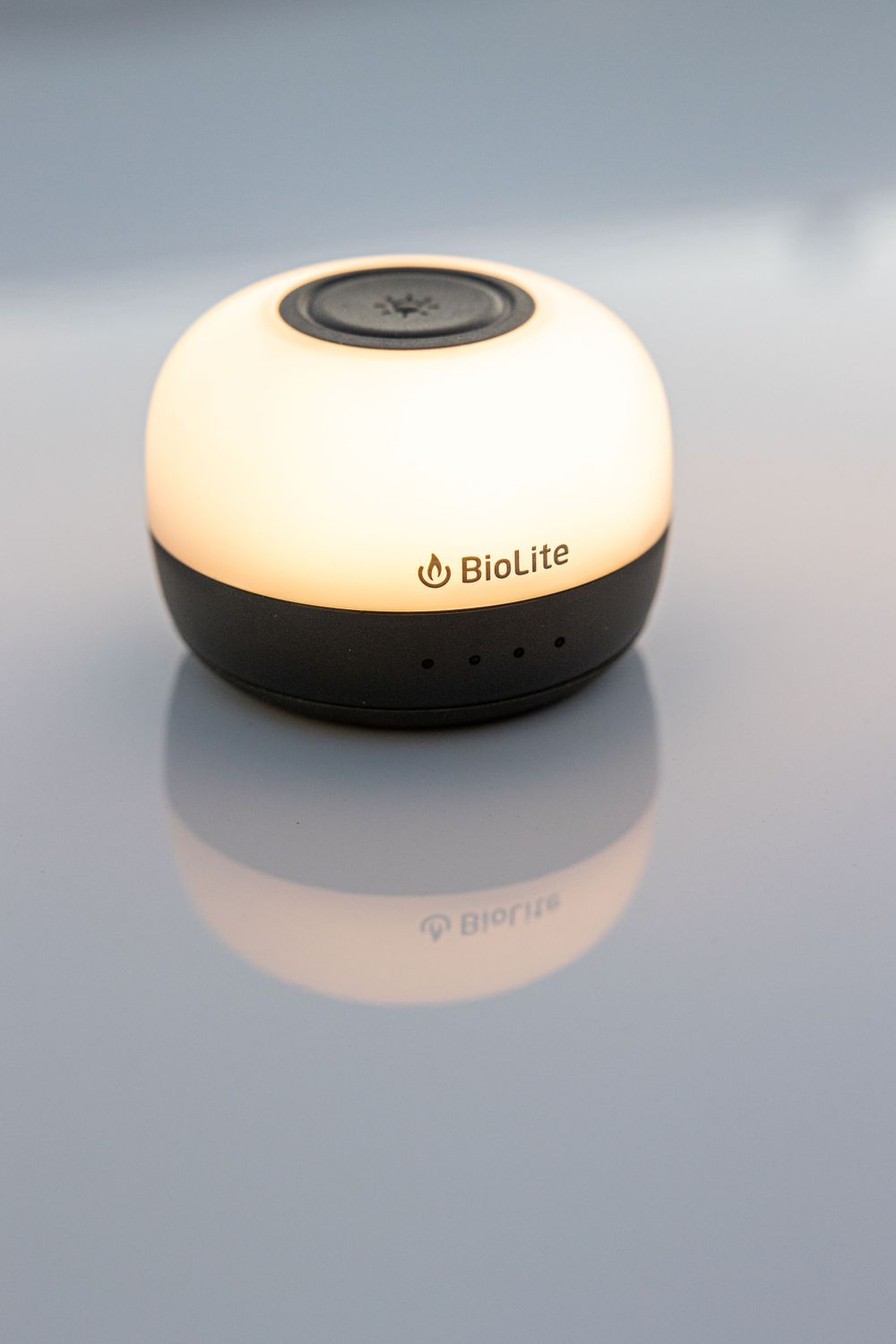 BioLite AlpenGlow camping lantern emitting warm white light on reflective surface.