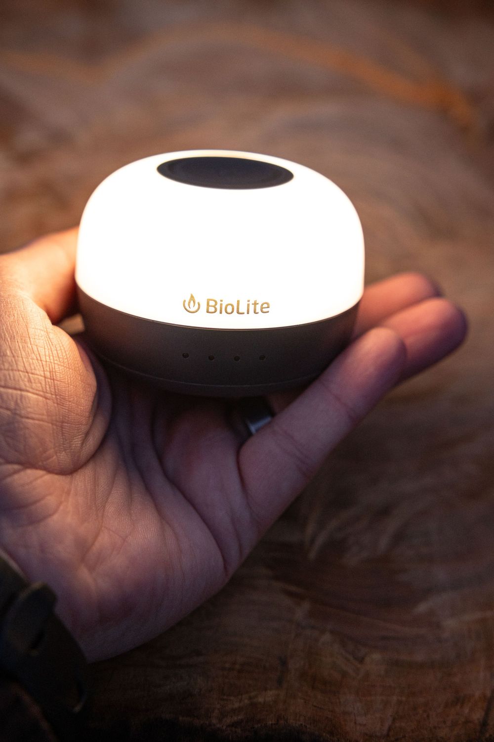 Hand holding illuminated white BioLite camping lantern against dark background.