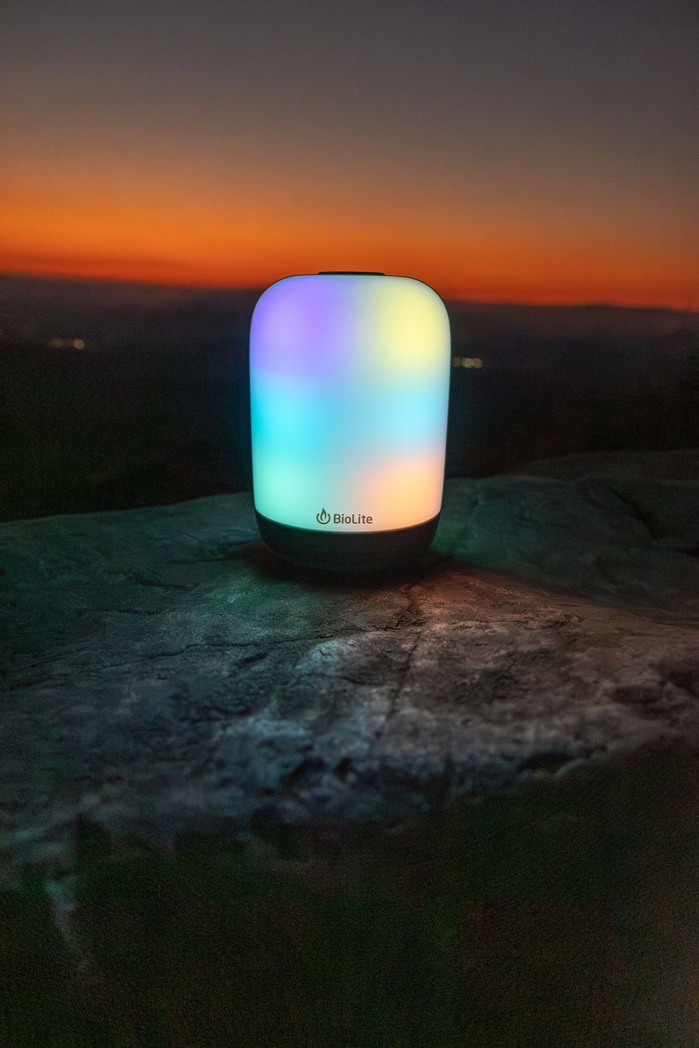 BioLite lantern displays multicolored LED lights on a rocky surface at dusk.