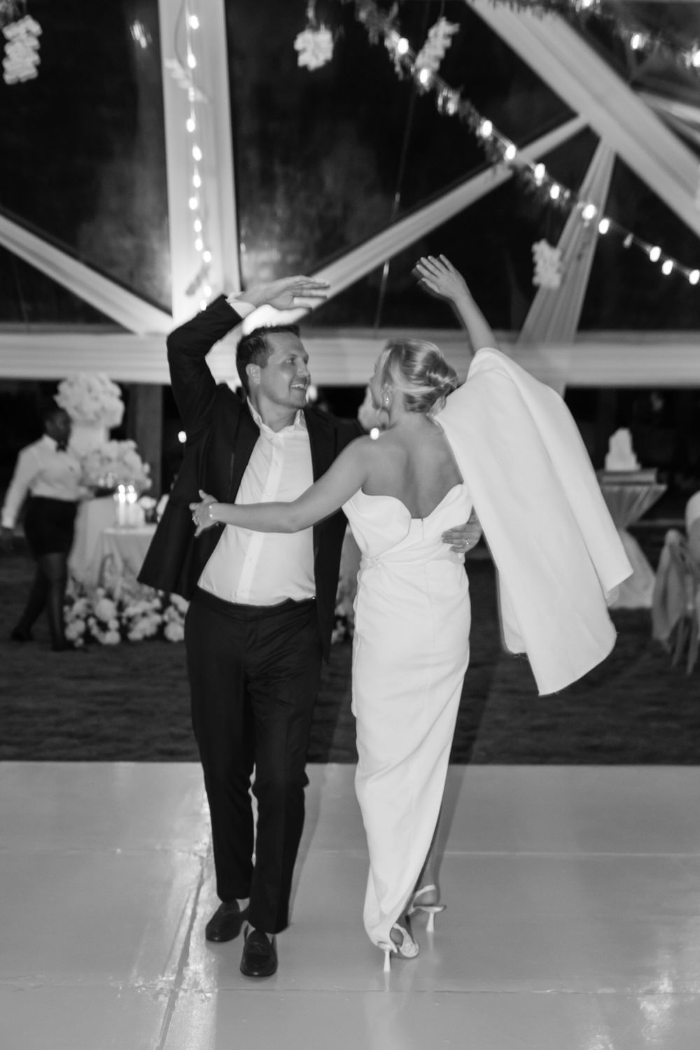 Black and white photo of dancing couple under string lights and tent draping.