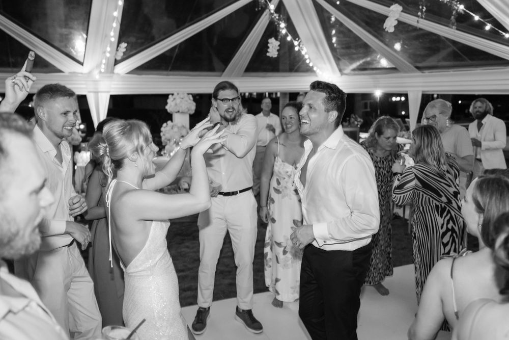Wedding guests dancing and celebrating at a lively reception under a tent with string lights.