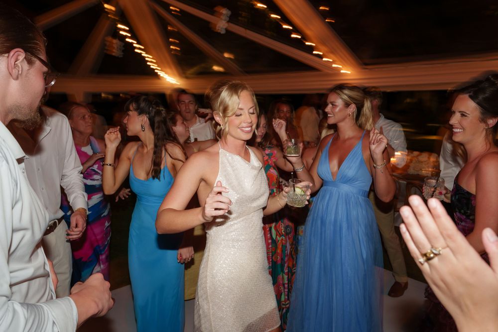 Wedding reception guests dancing and celebrating on a lively dance floor with colorful dresses and string lights overhead.