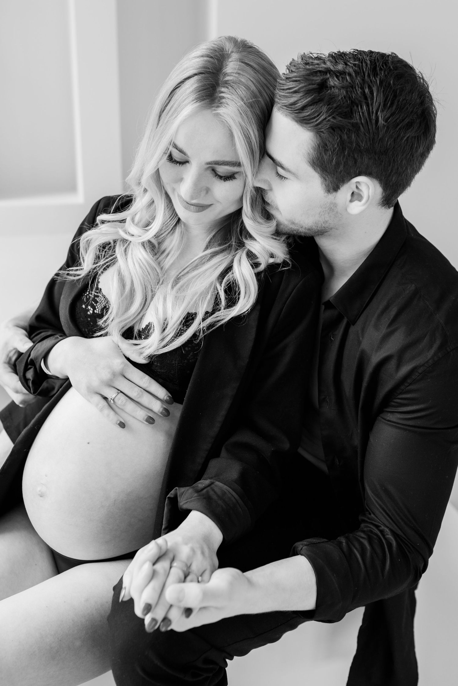 Black and white intimate maternity photo showing couple in tender moment with hands resting on pregnant belly.