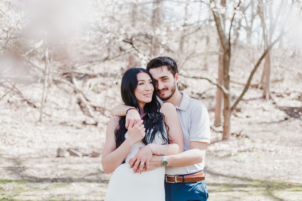 A romantic engagement photo shoot outdoors featuring an embracing couple in casual attire against a natural background.