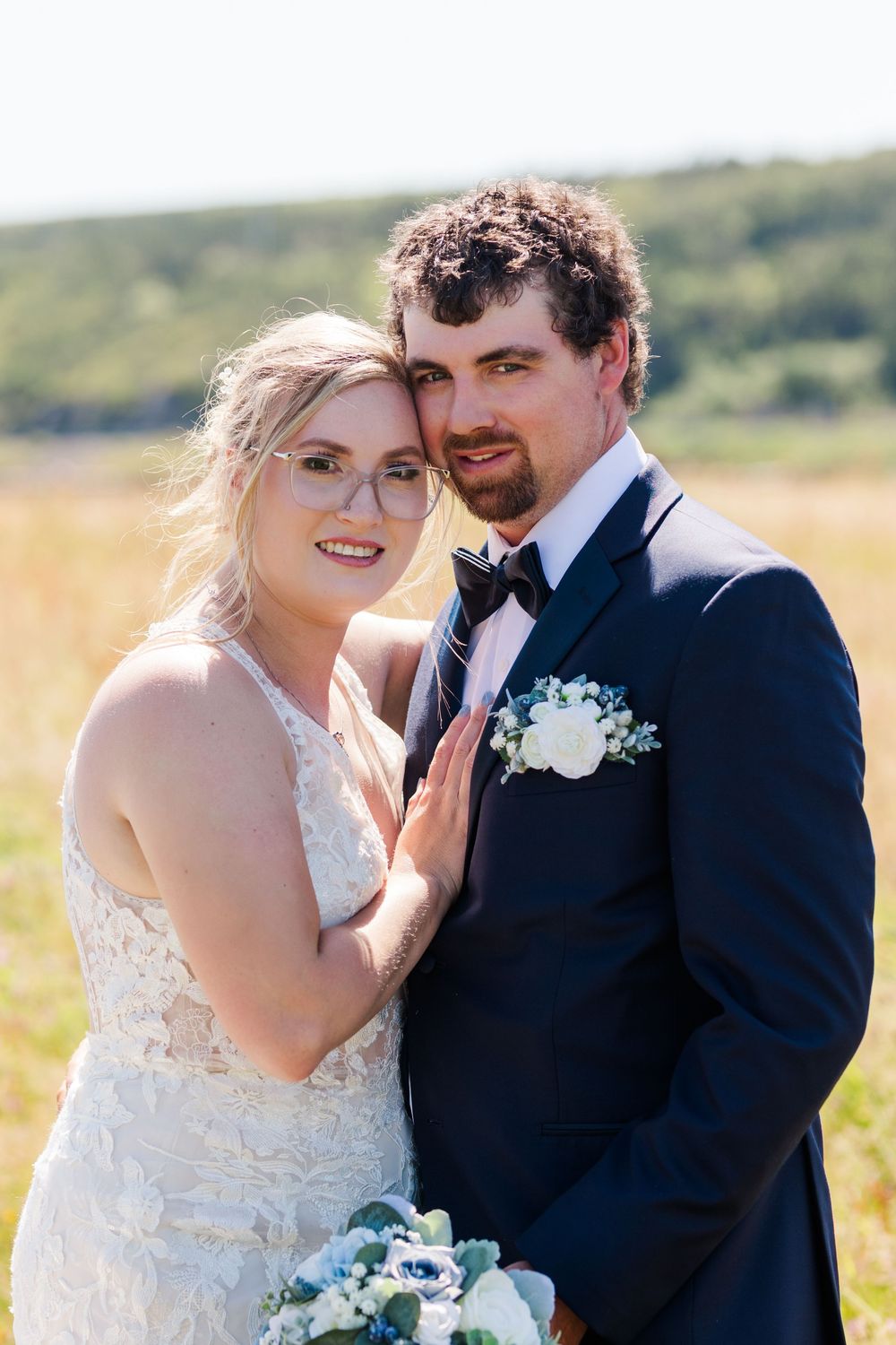 Wedding couple shares tender moments in a sunny meadow wearing traditional white dress and dark suit.
