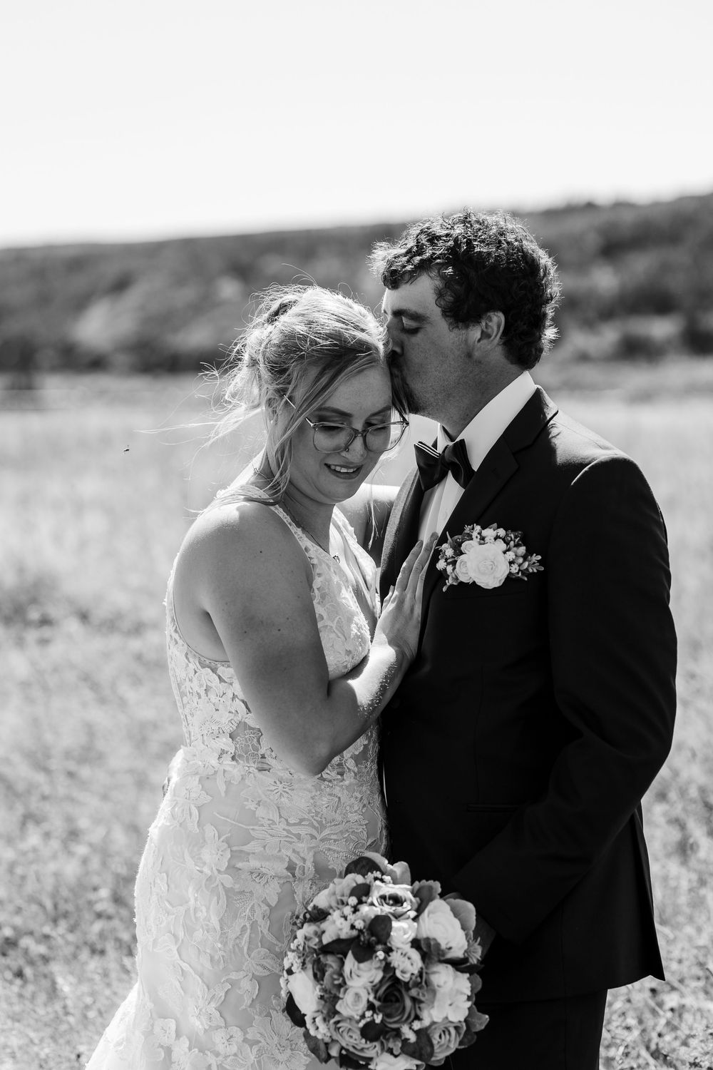 A romantic black and white wedding portrait of a couple laughing together in a grassy outdoor field.