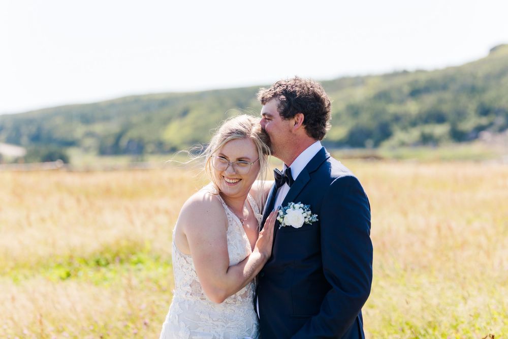A romantic wedding couple shares a passionate embrace while standing in a sunlit golden field.
