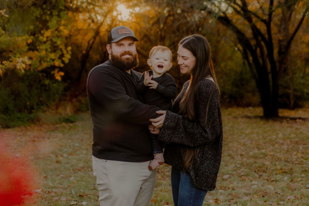 A family shares joyful laughter together during an autumn photo session with golden foliage in the background.