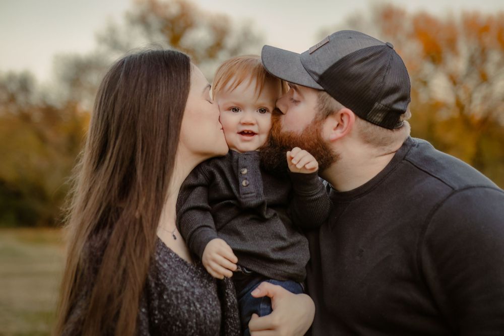 A family shares a tender moment together outdoors during autumn with fall foliage in the background.