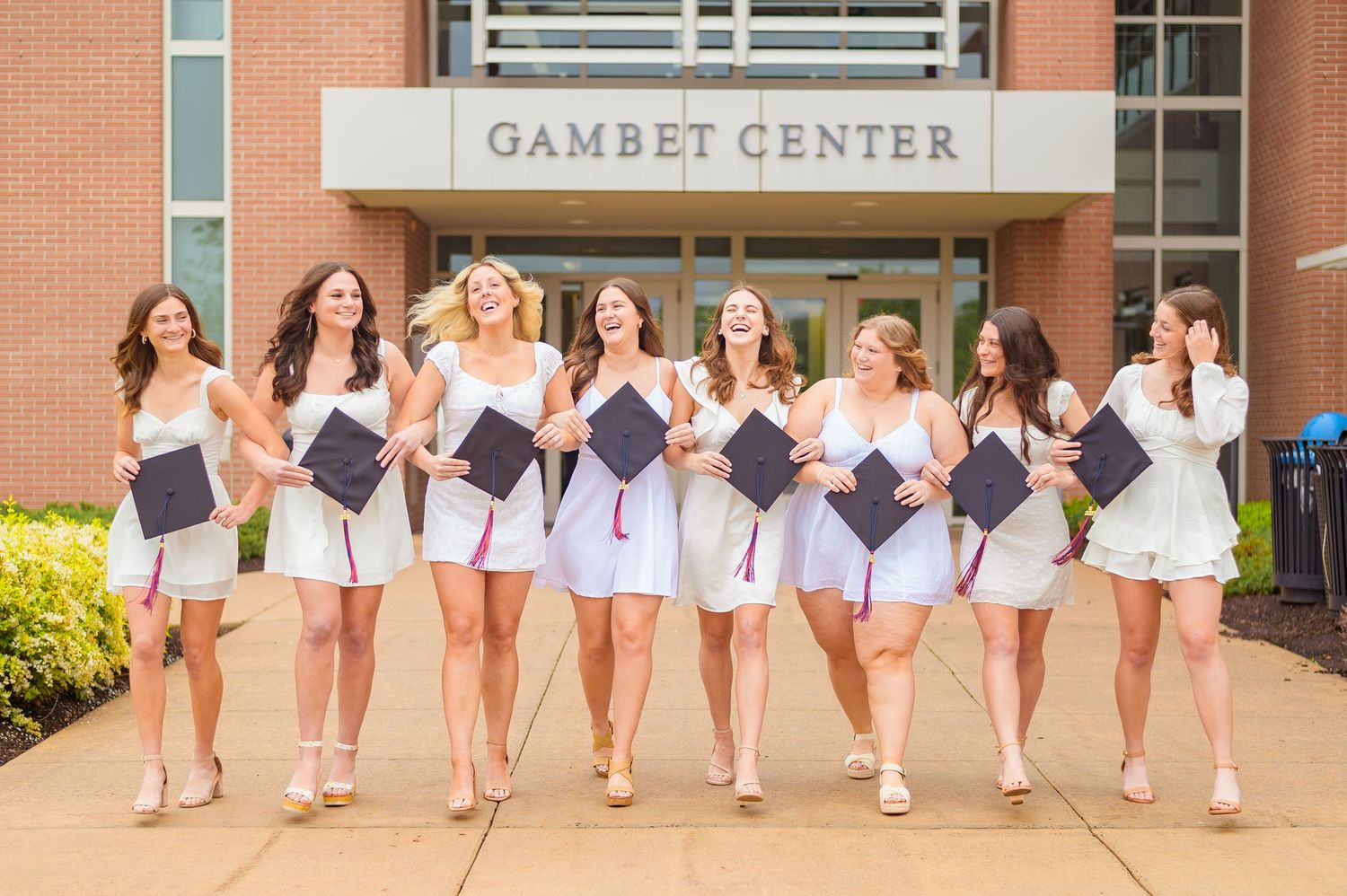 A line of graduates in white dresses pose outside the Gambet Center building.