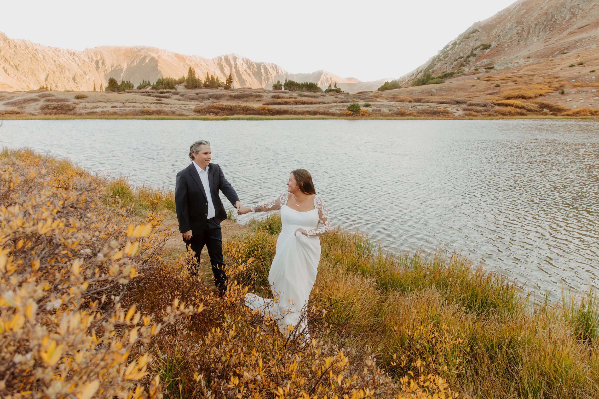Couple stands together near scenic mountain lake during sunset photography session.