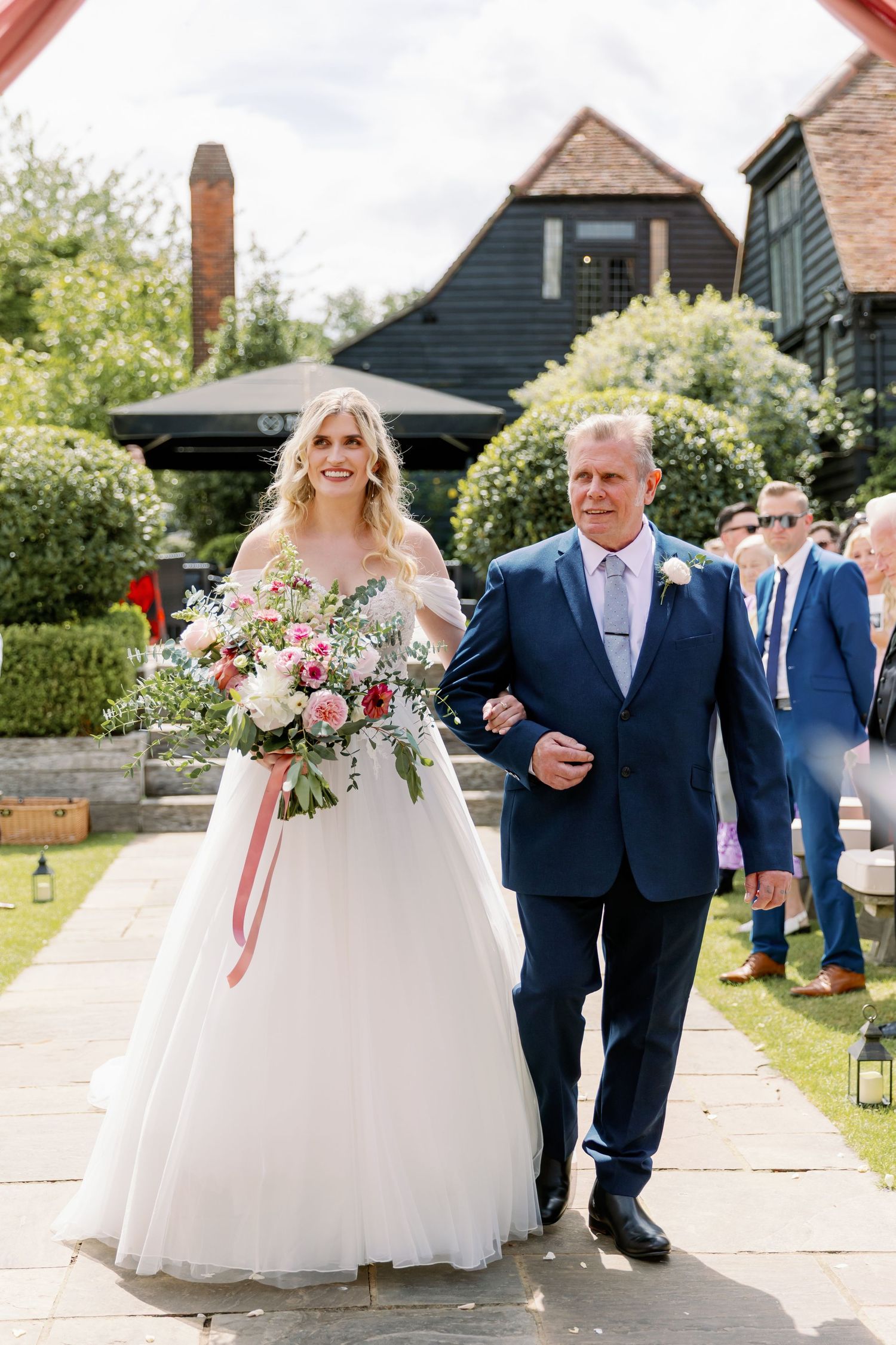 A joyful wedding processional on a stone path with blue-suited attendants and a flowing white ballgown.