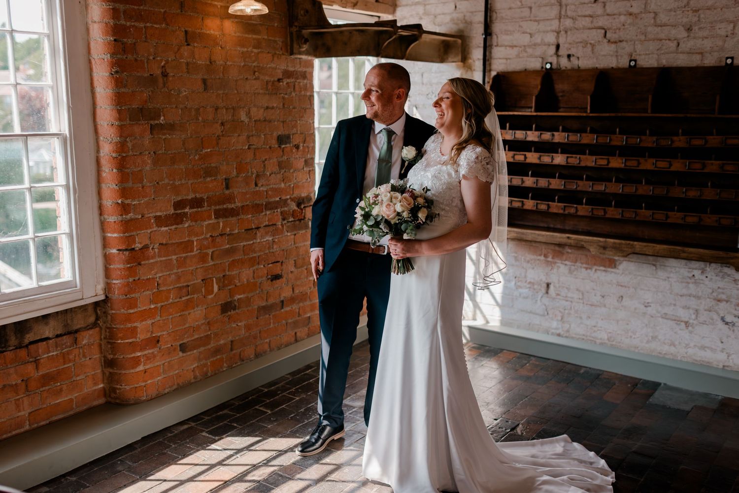 Wedding couple shares intimate moments in a rustic brick venue with natural window lighting.