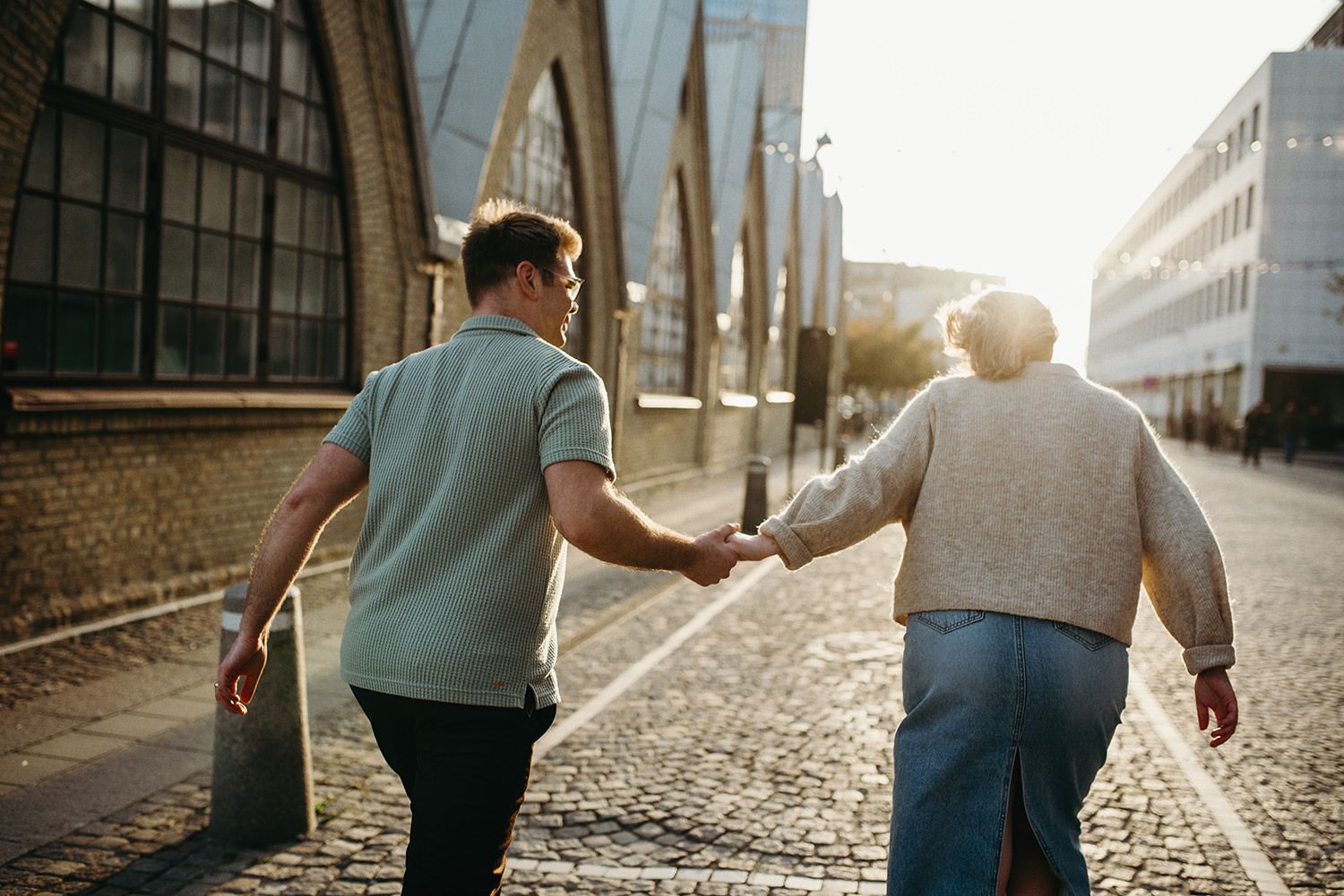 Two people walking together holding hands on a cobblestone street during golden hour sunlight.