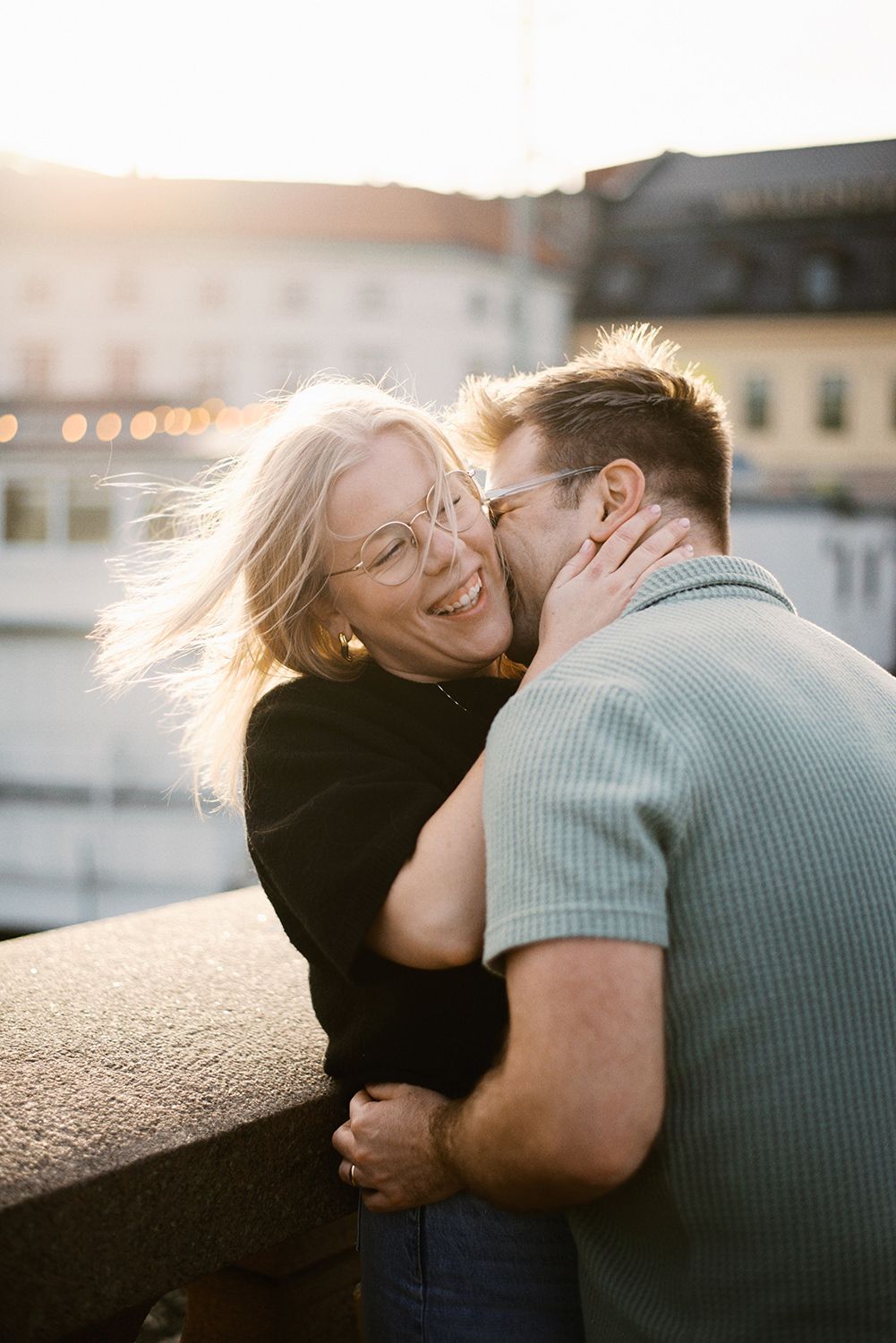 A joyful couple shares an intimate moment on a rooftop at sunset while bathed in golden hour light.
