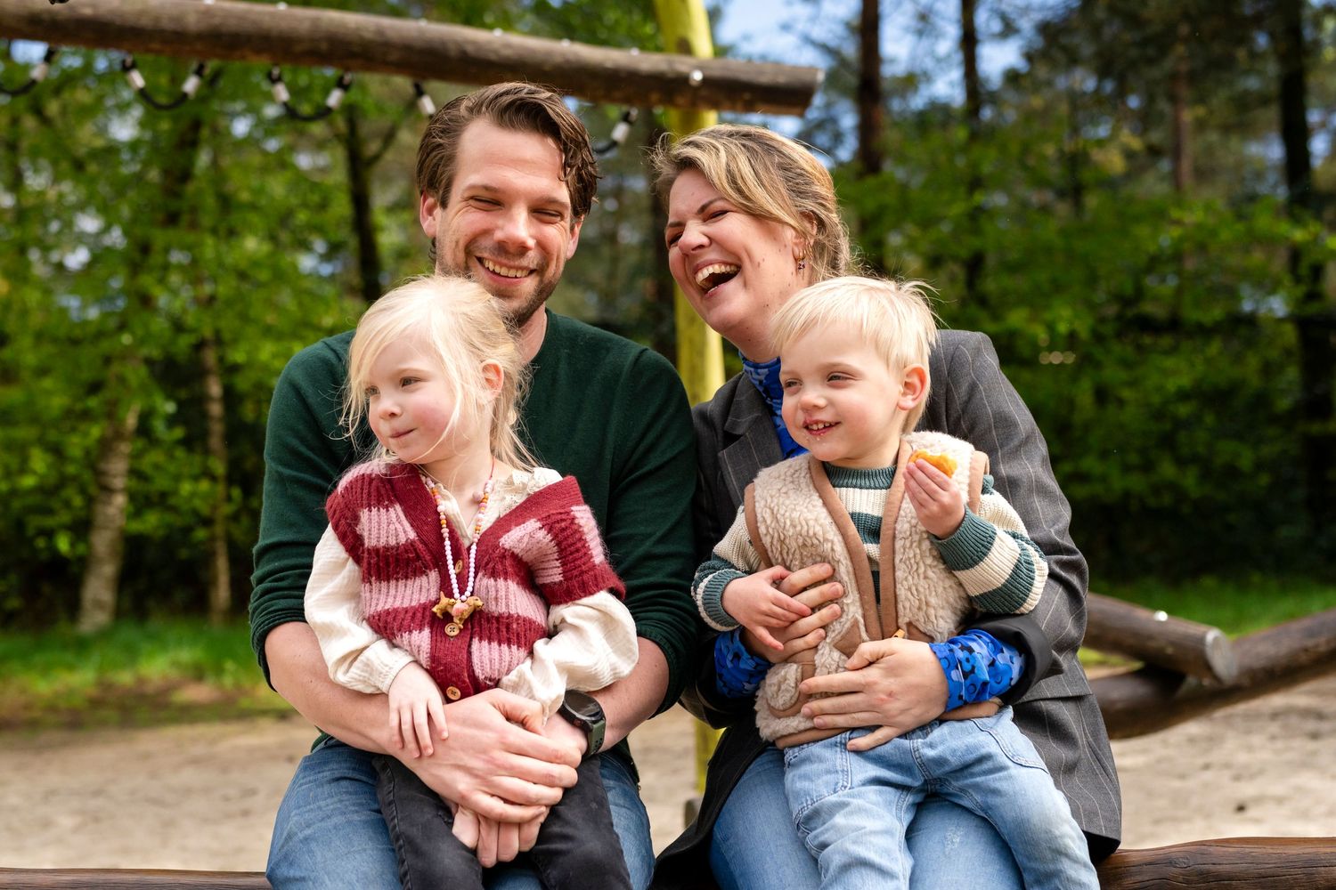 Happy family with two young children enjoying a playful moment outdoors in a park setting.