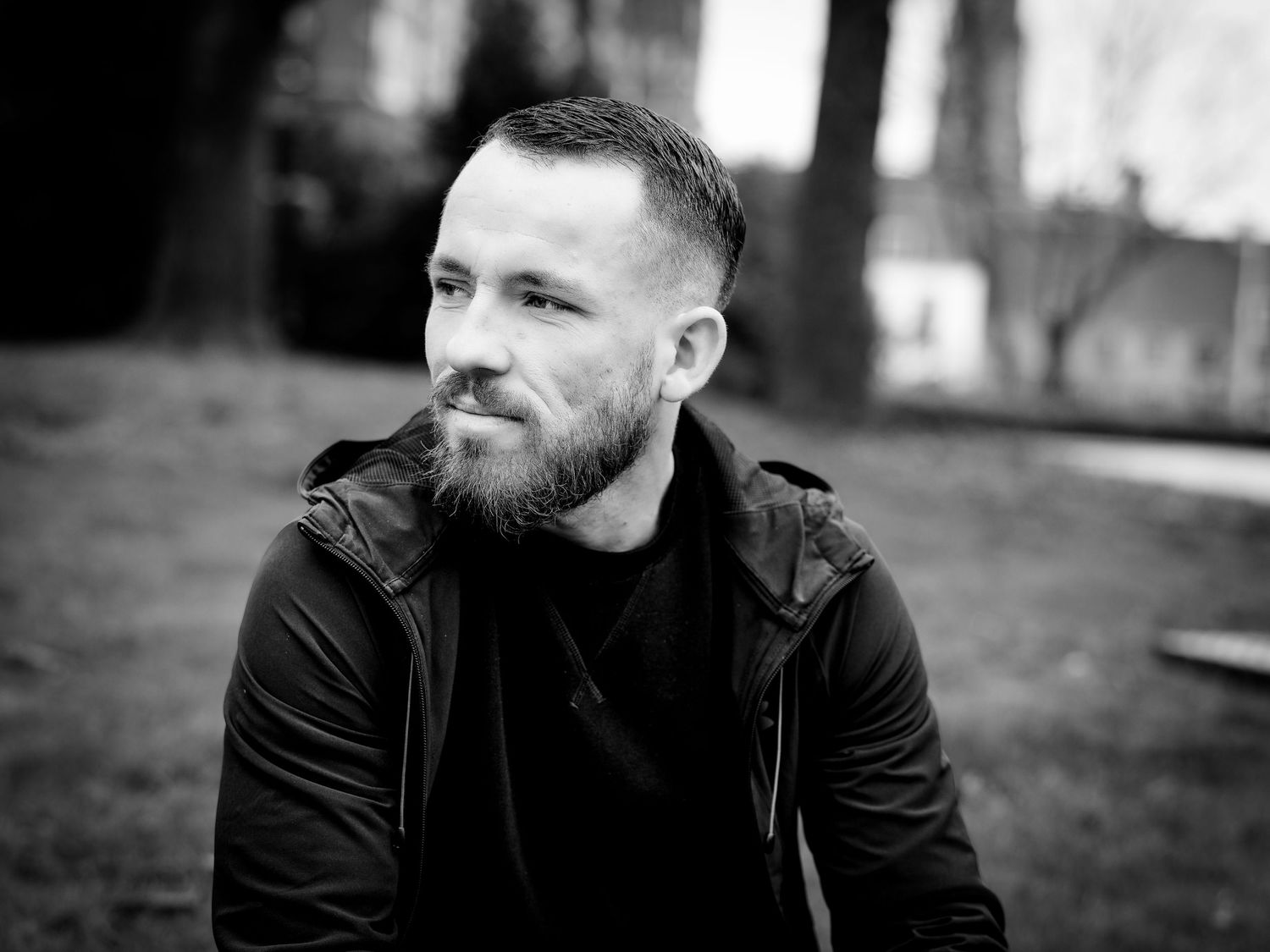 Black and white portrait of bearded man in dark jacket outdoors.
