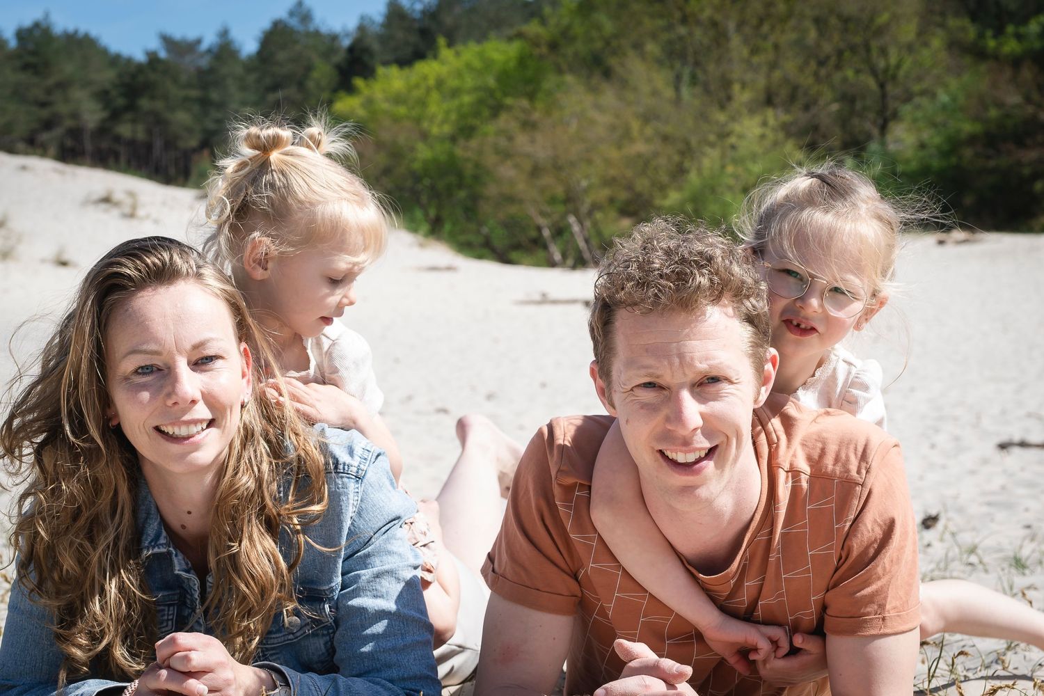Candid portrait of family members laughing together on beach sand.
