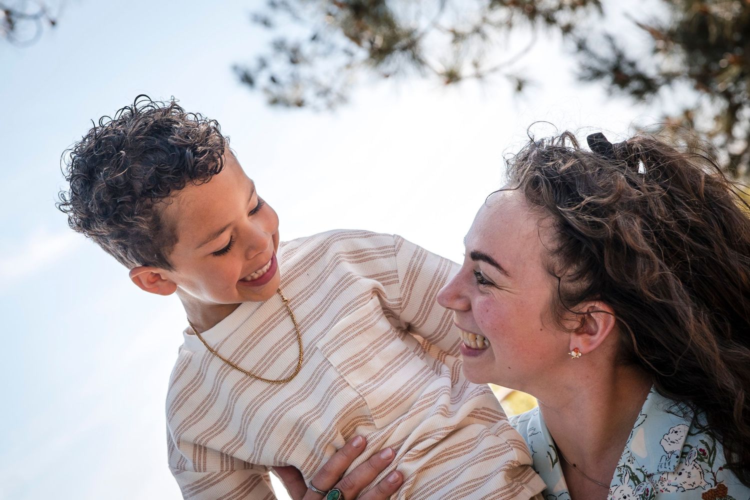 Joyful candid moment captured between parent and child against bright sky background.