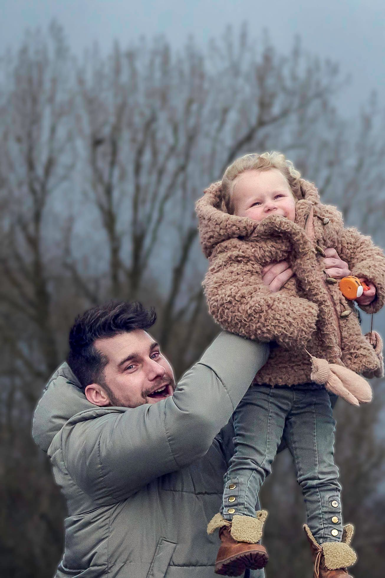 Playful moment captured outdoors with cozy teddy coat and winter attire against bare trees.