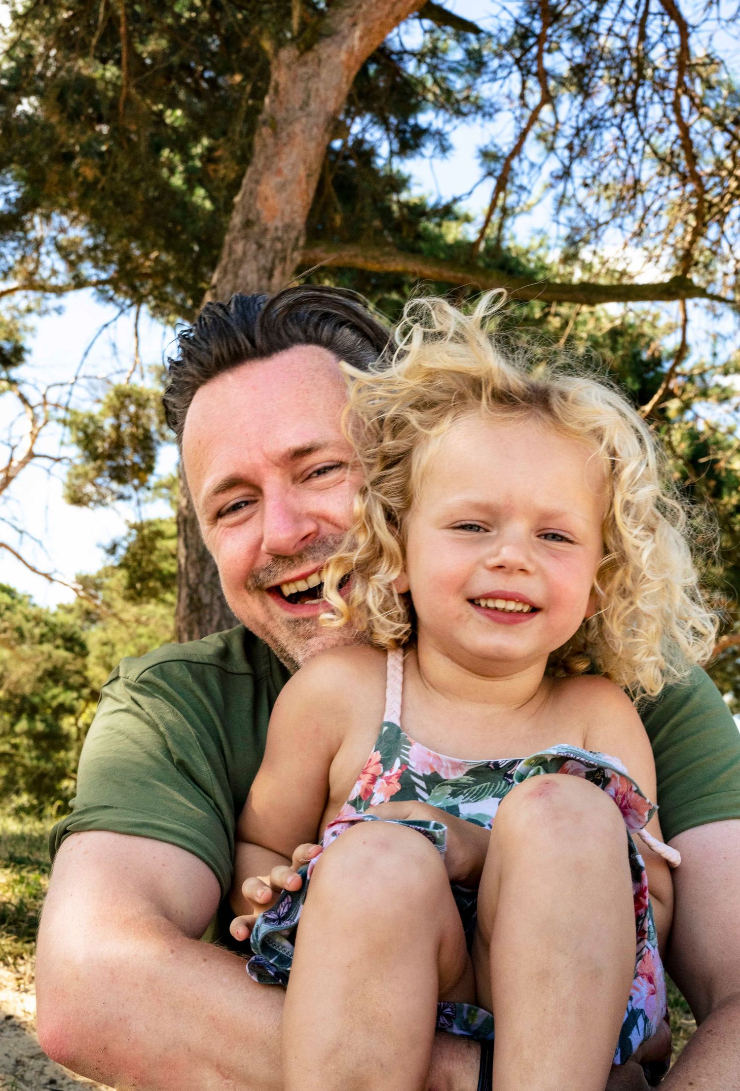 A heartwarming outdoor portrait showing pure joy and laughter under a sunlit tree.