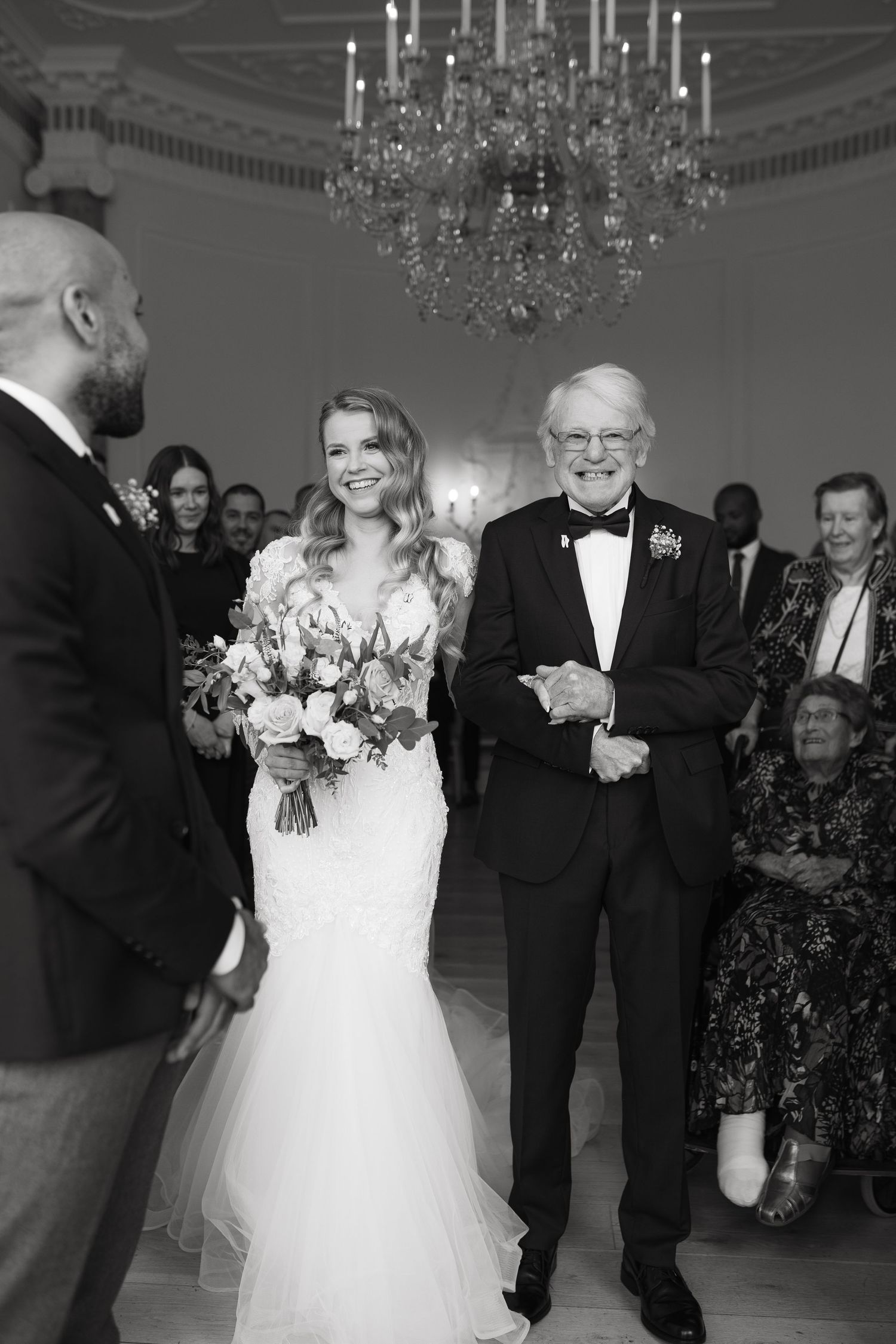 Elegant wedding reception features dancing between father and daughter in white dress under crystal chandeliers.