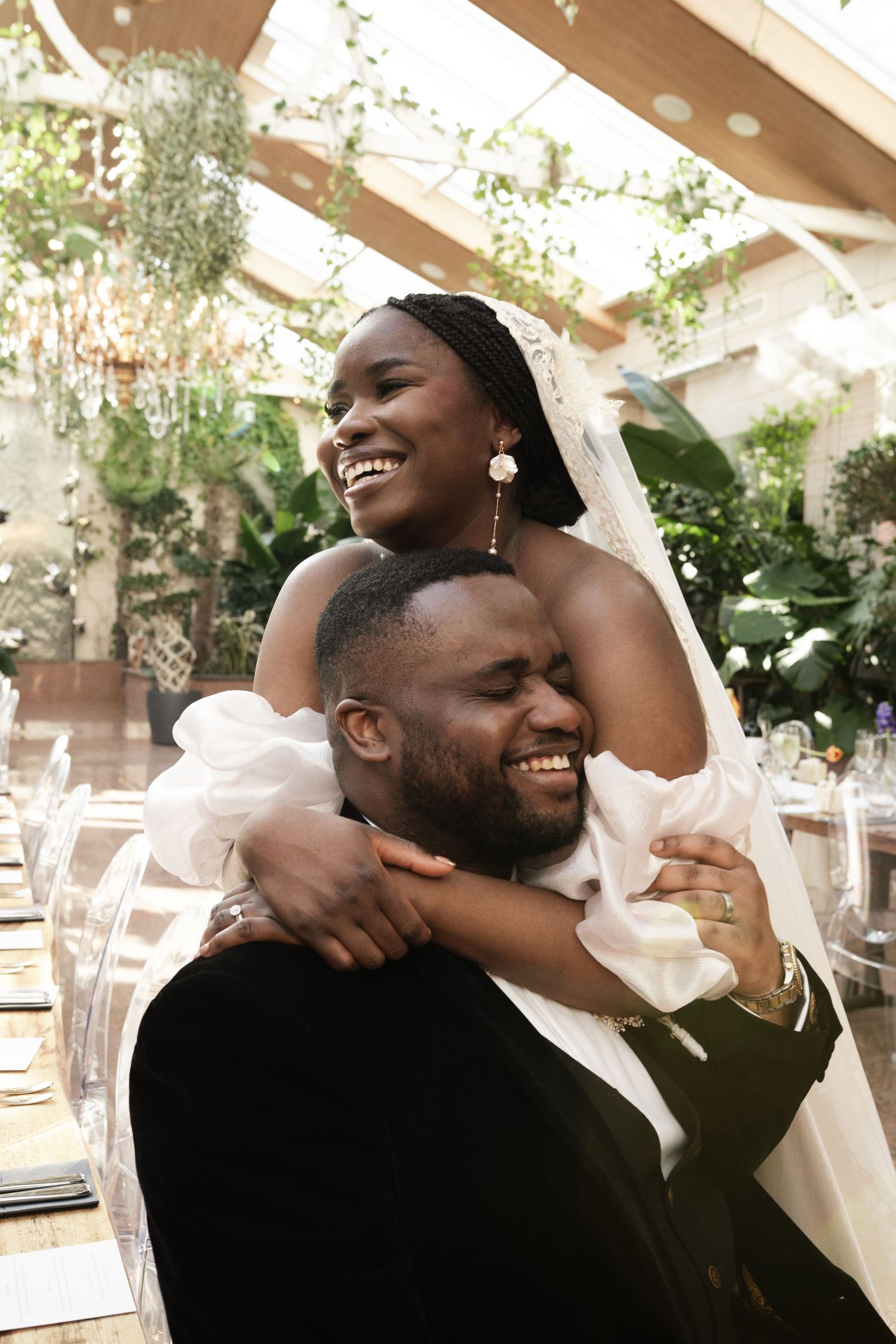 Joyful bride and groom share intimate laughing moment at sunlit indoor wedding reception.