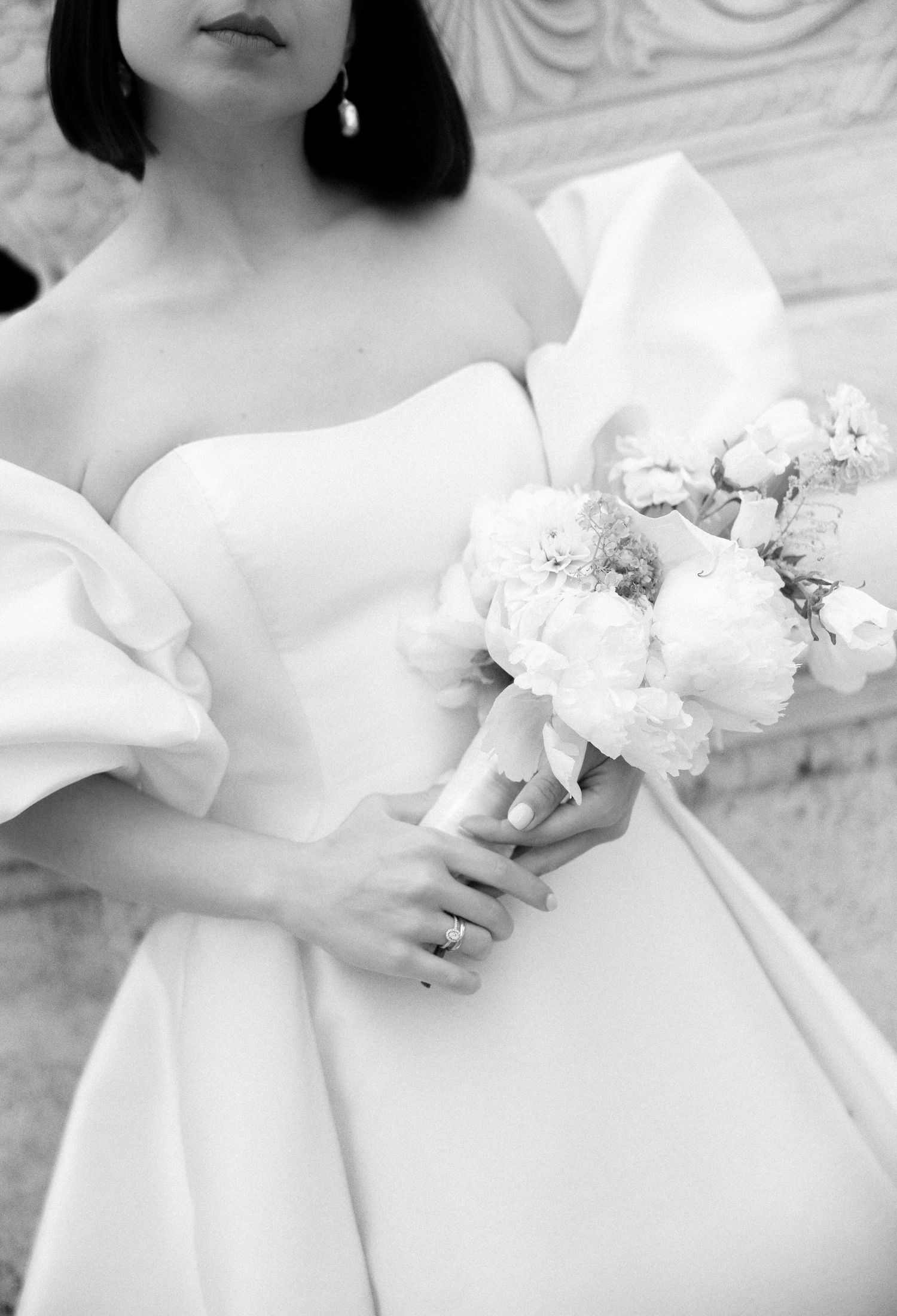 Close-up of a bridal gown with a white bouquet of flowers against a classic backdrop.