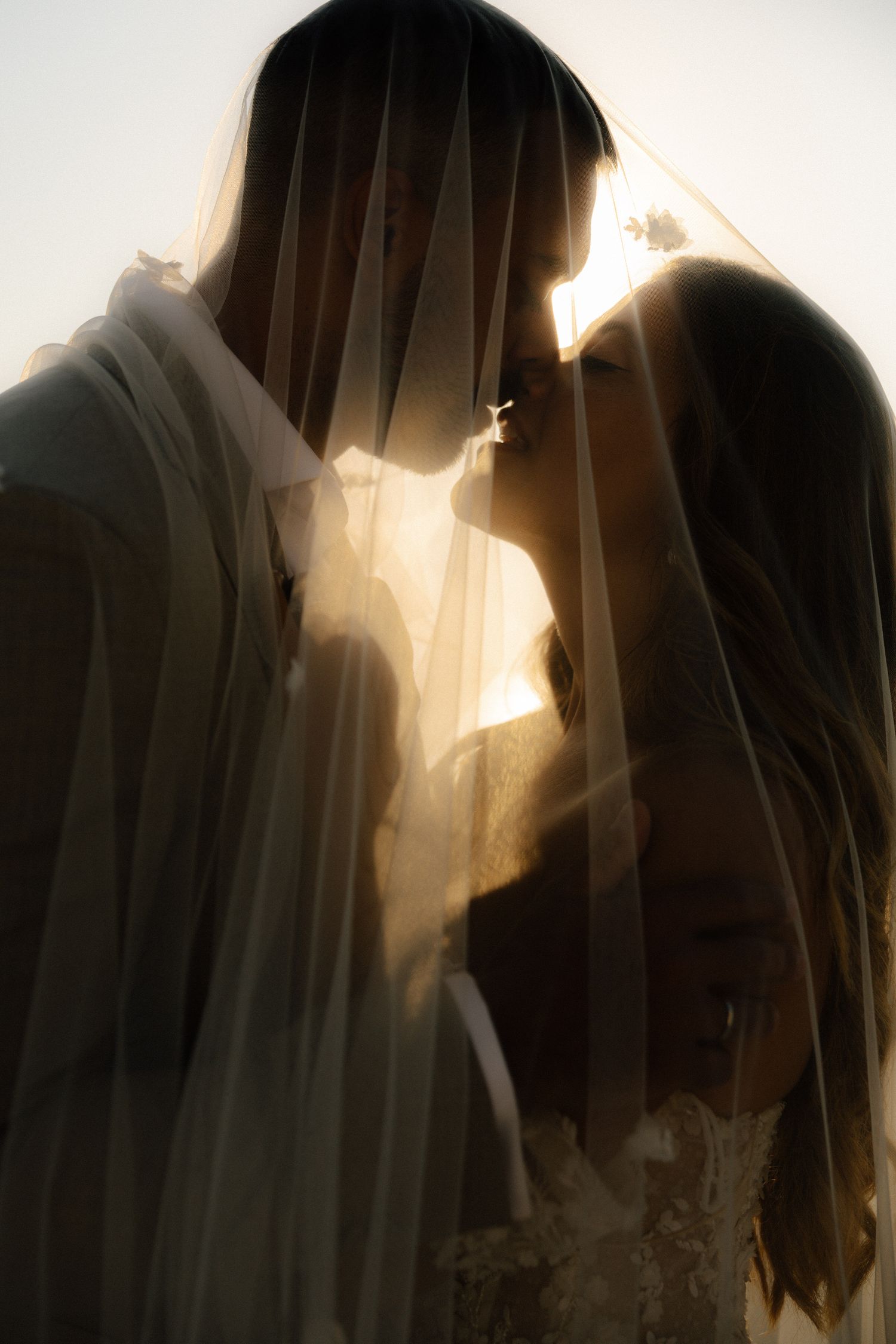 An artistic sepia-toned portrait of a couple in wedding attire with backlit veils.