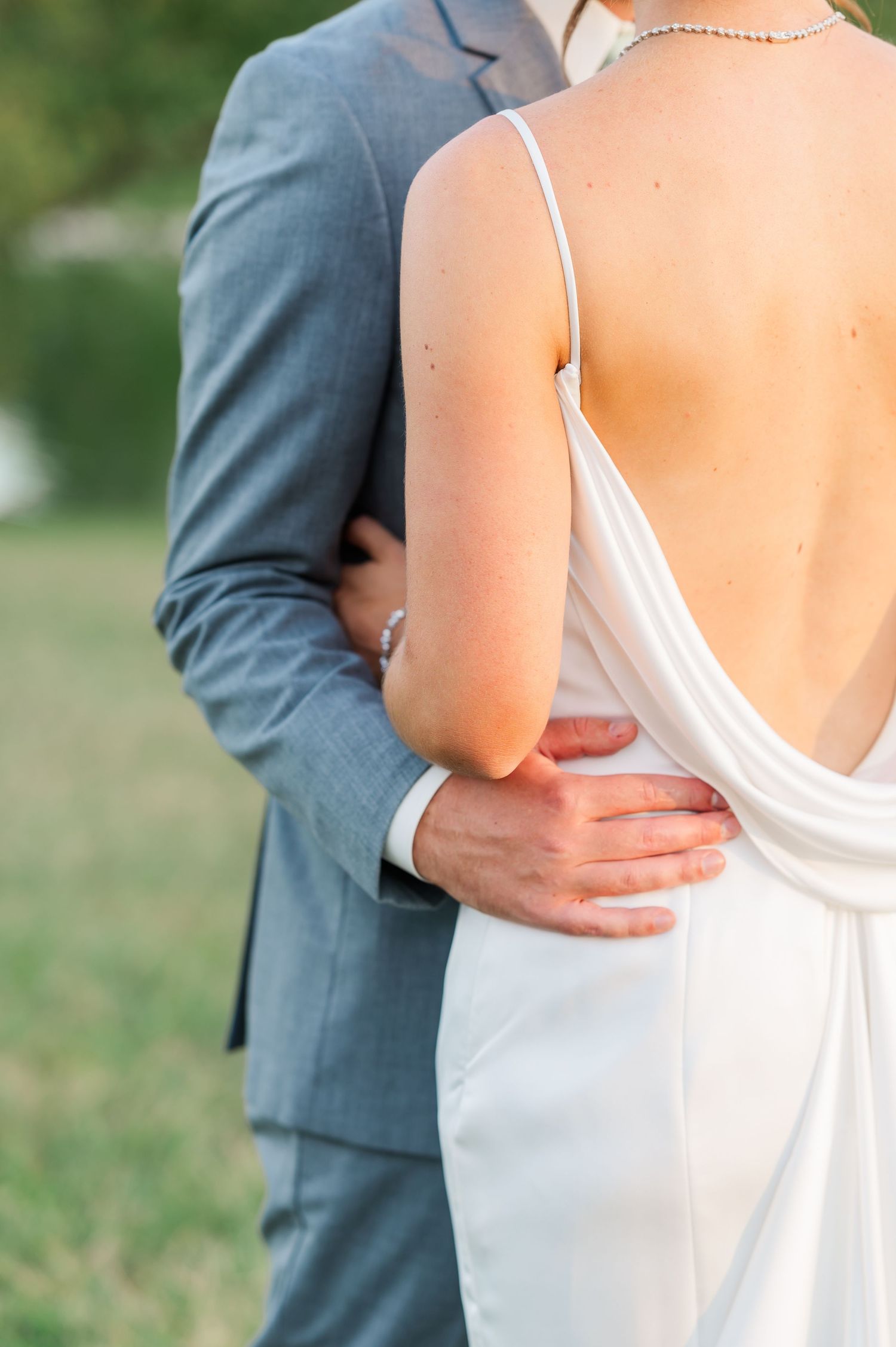 closeup of groom holding bride around the waist with the Wedding dress having a low draped back