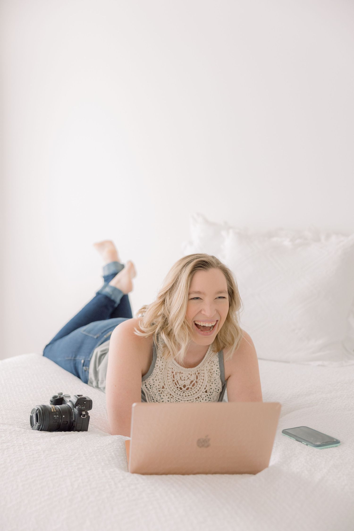 Stephanie Wade laying on bed with laptop and camera smiling