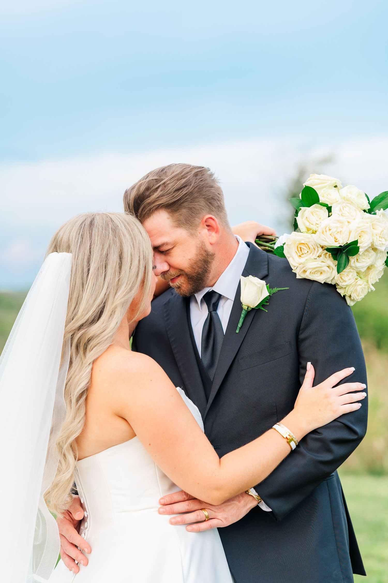 bride and groom forehead to forehead with a bouquet over the grooms back