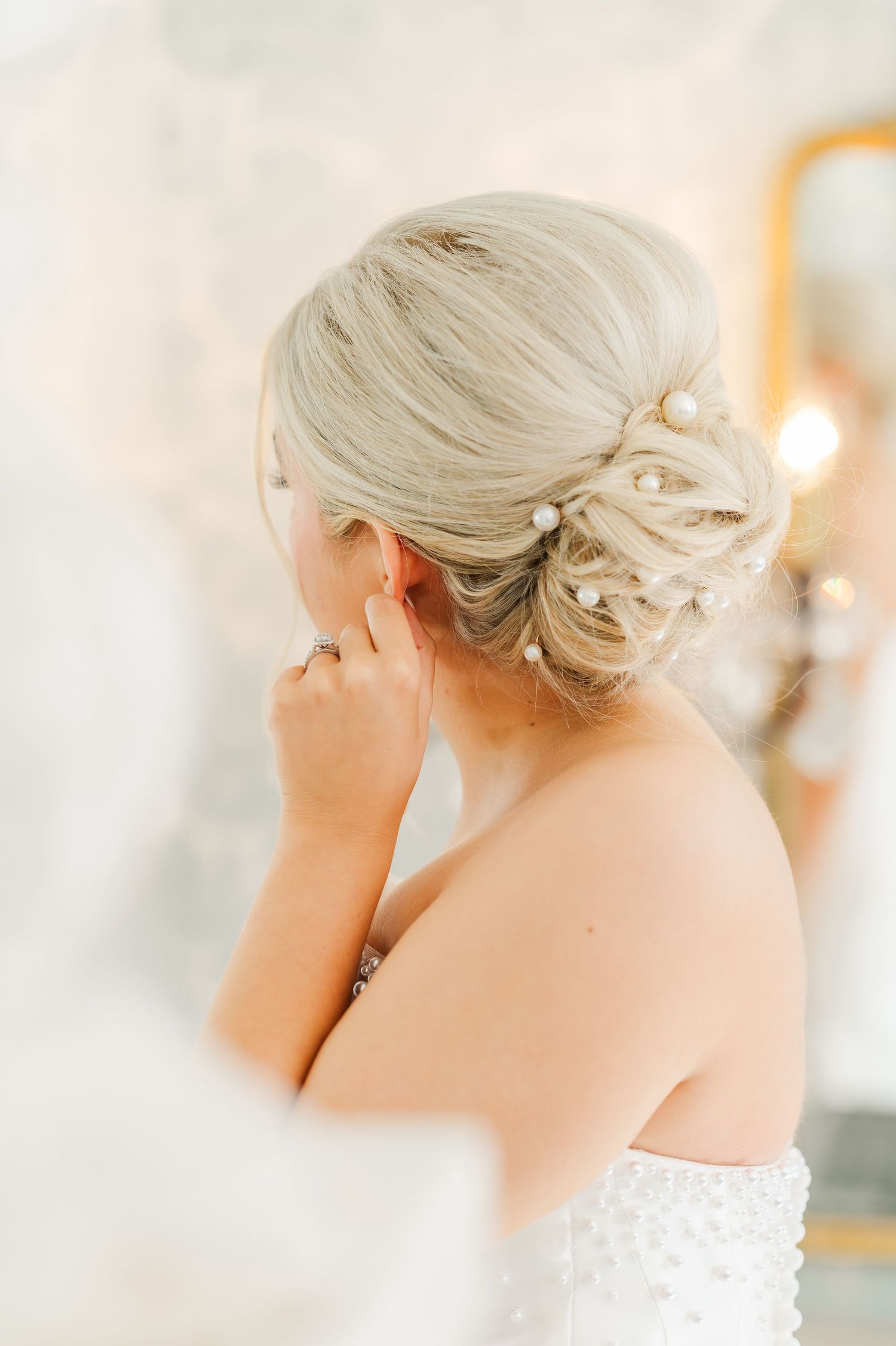 back of brides head showing off her bridal hair with pear pins laced throughout the bun while fixing her earring