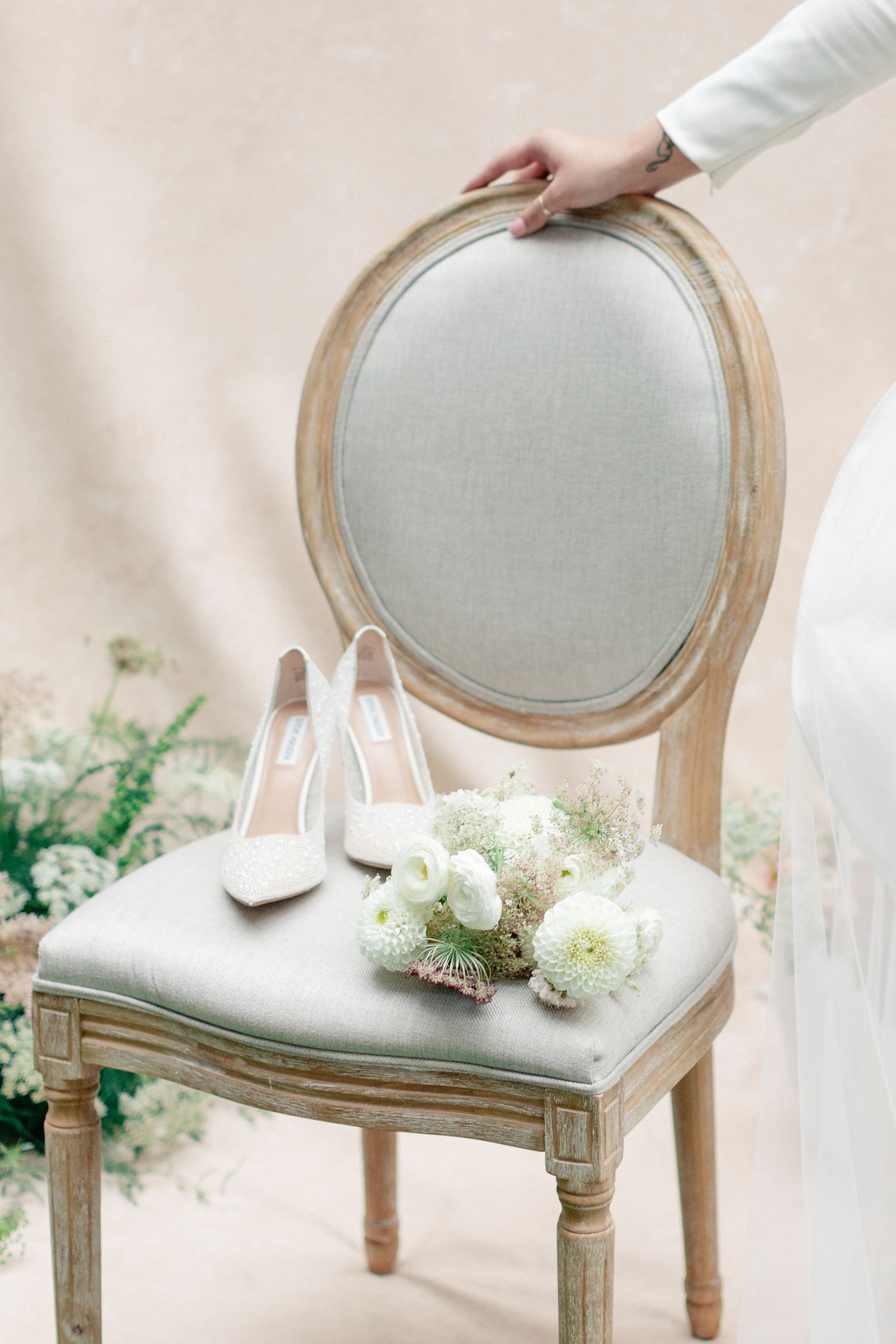 White heels and flowers arranged on an elegant French-style gray chair.