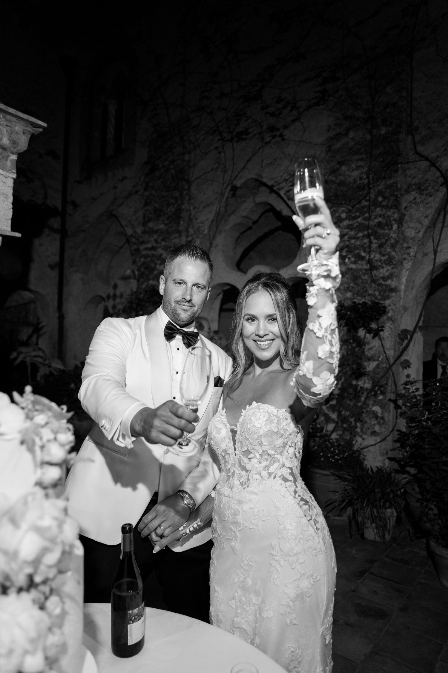 A bride and groom toasting with champagne glasses at their wedding reception in a dimly lit venue with stone walls.