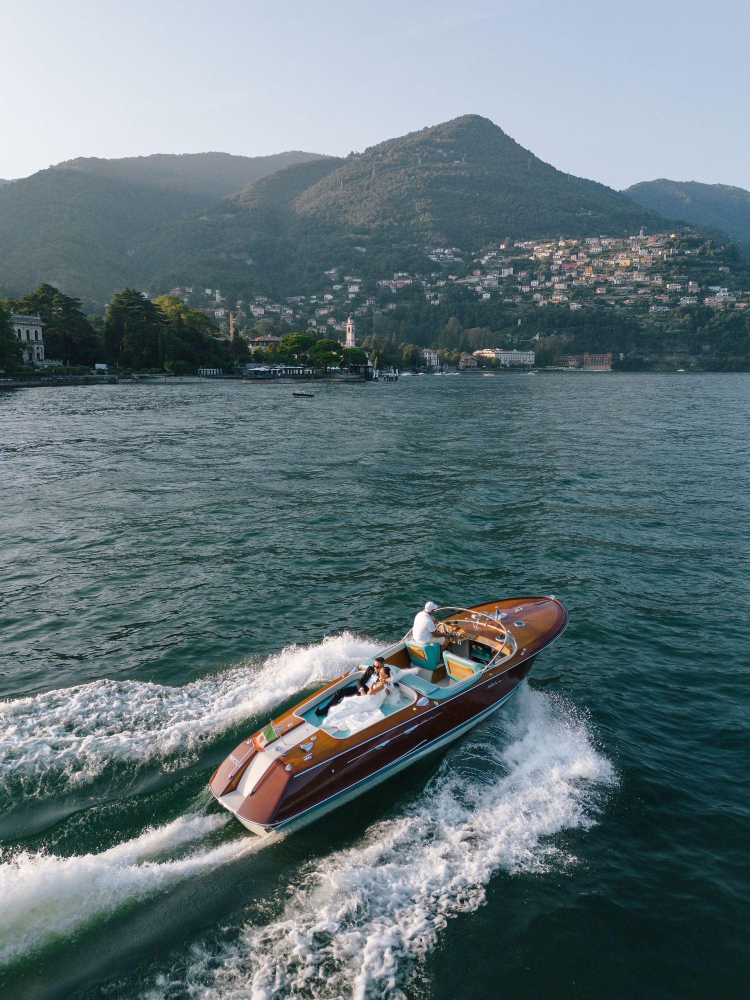 Vintage wooden Riva boat speeding across Lake Como with mountains and lakeside villas in the background.