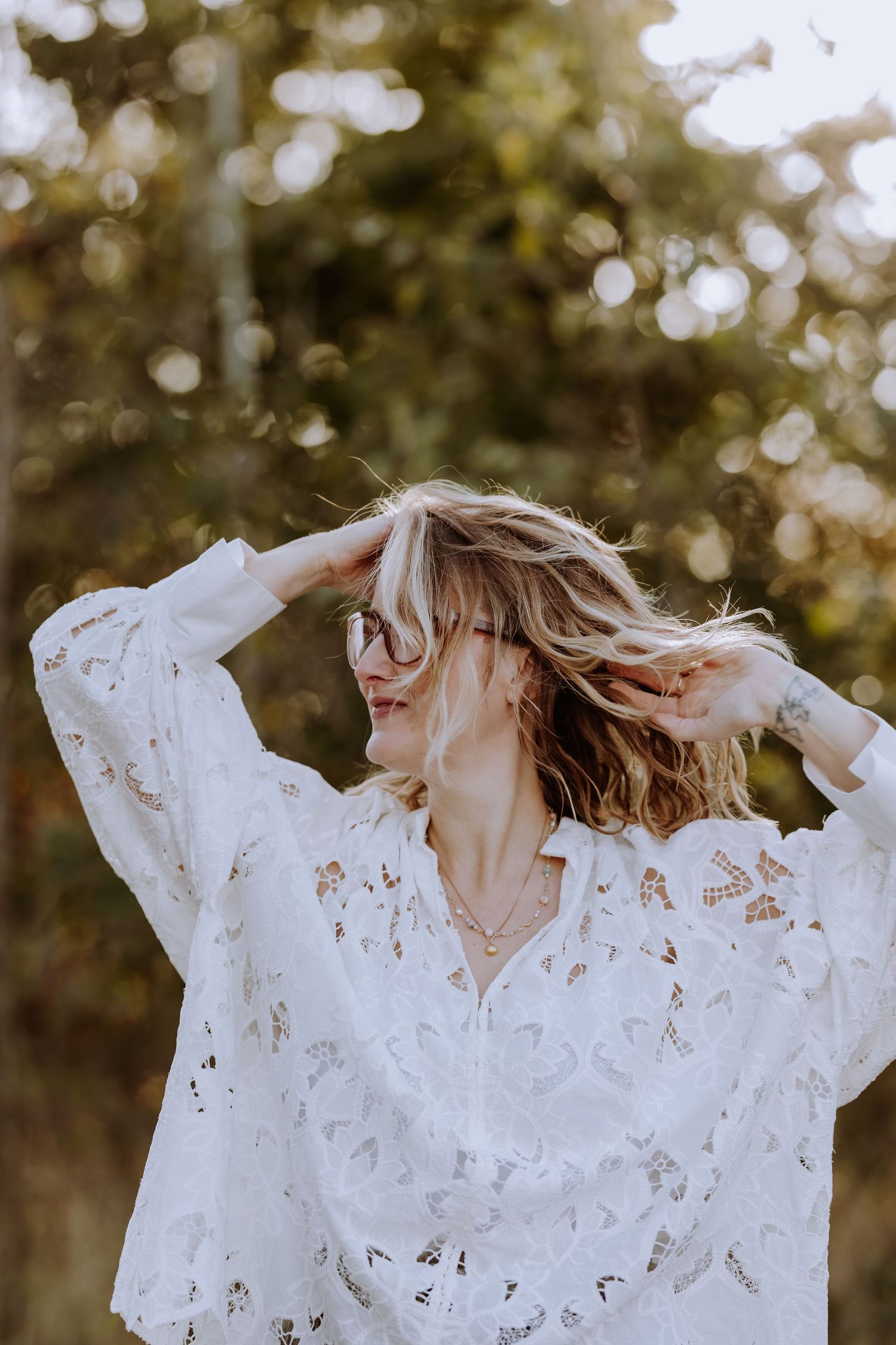 A person in a white lace top dances in golden sunlight with windswept hair.