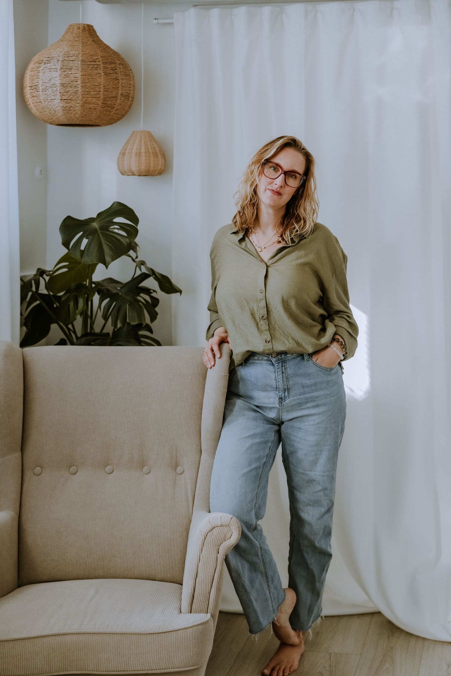 Casual lifestyle photo with beige armchair, woven pendant lamps and monstera plant decor.