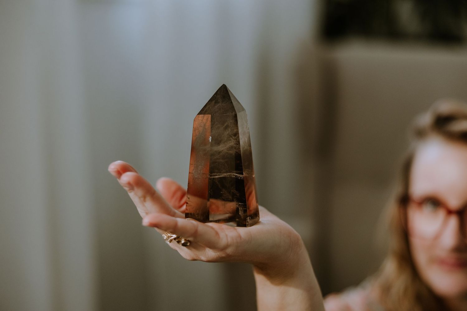 A hand holds up a large smoky quartz crystal point against a blurred background.