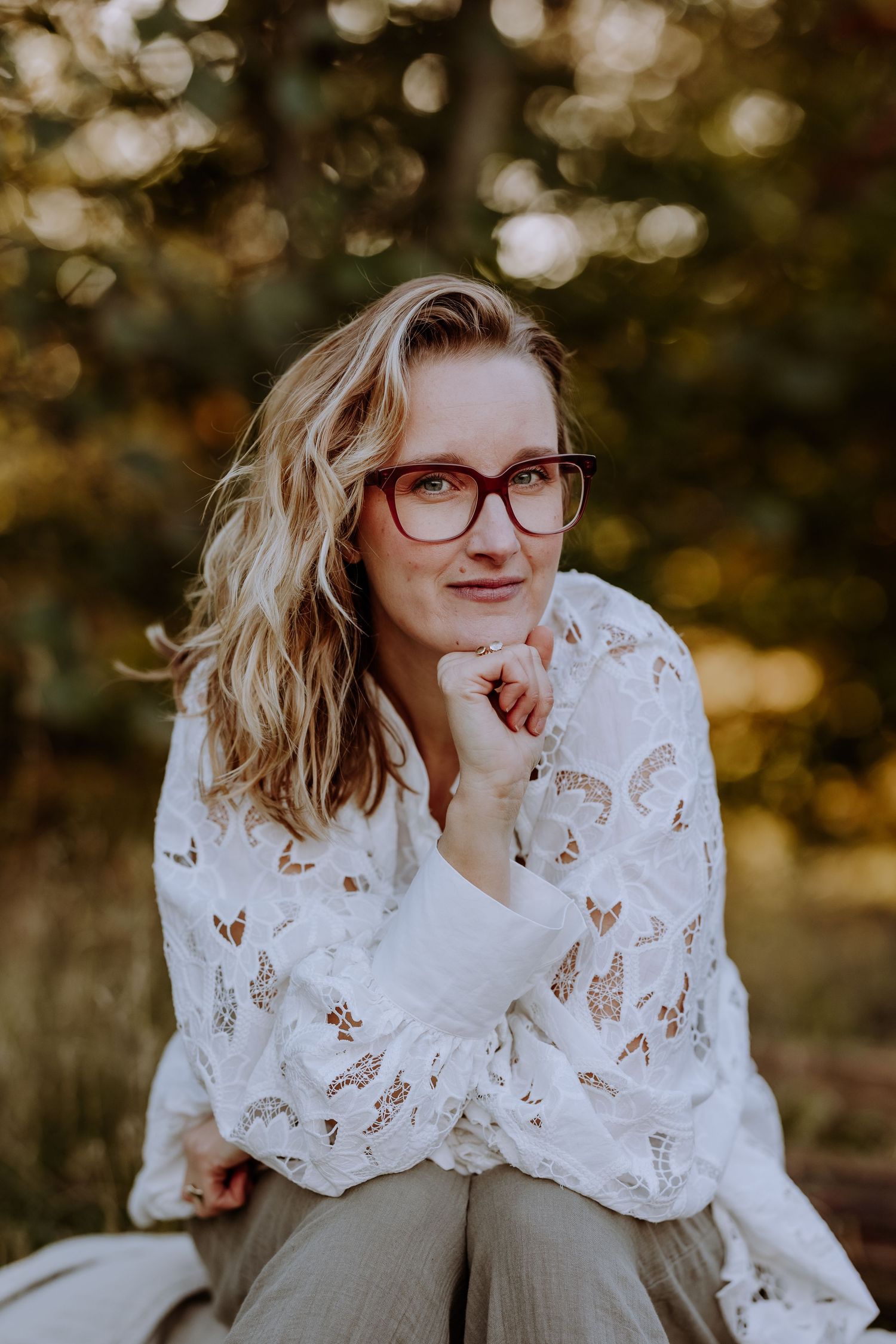 Portrait of someone in glasses and a white lace top posing thoughtfully against autumn bokeh background.