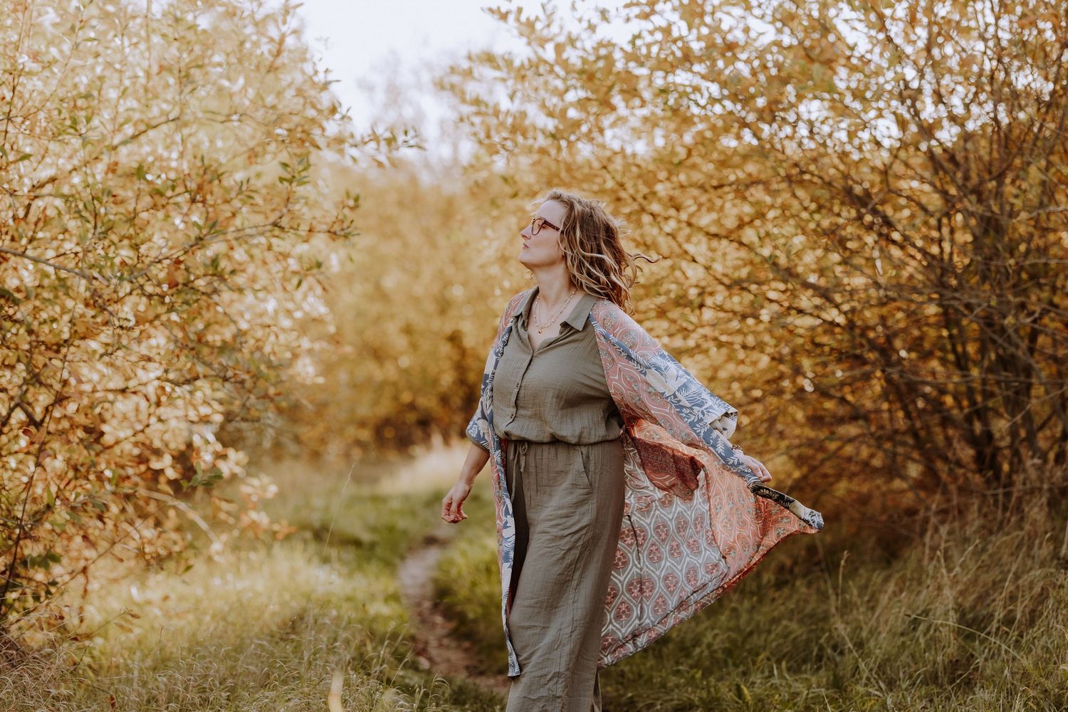 Someone in flowing clothing spins playfully on an autumn nature path.
