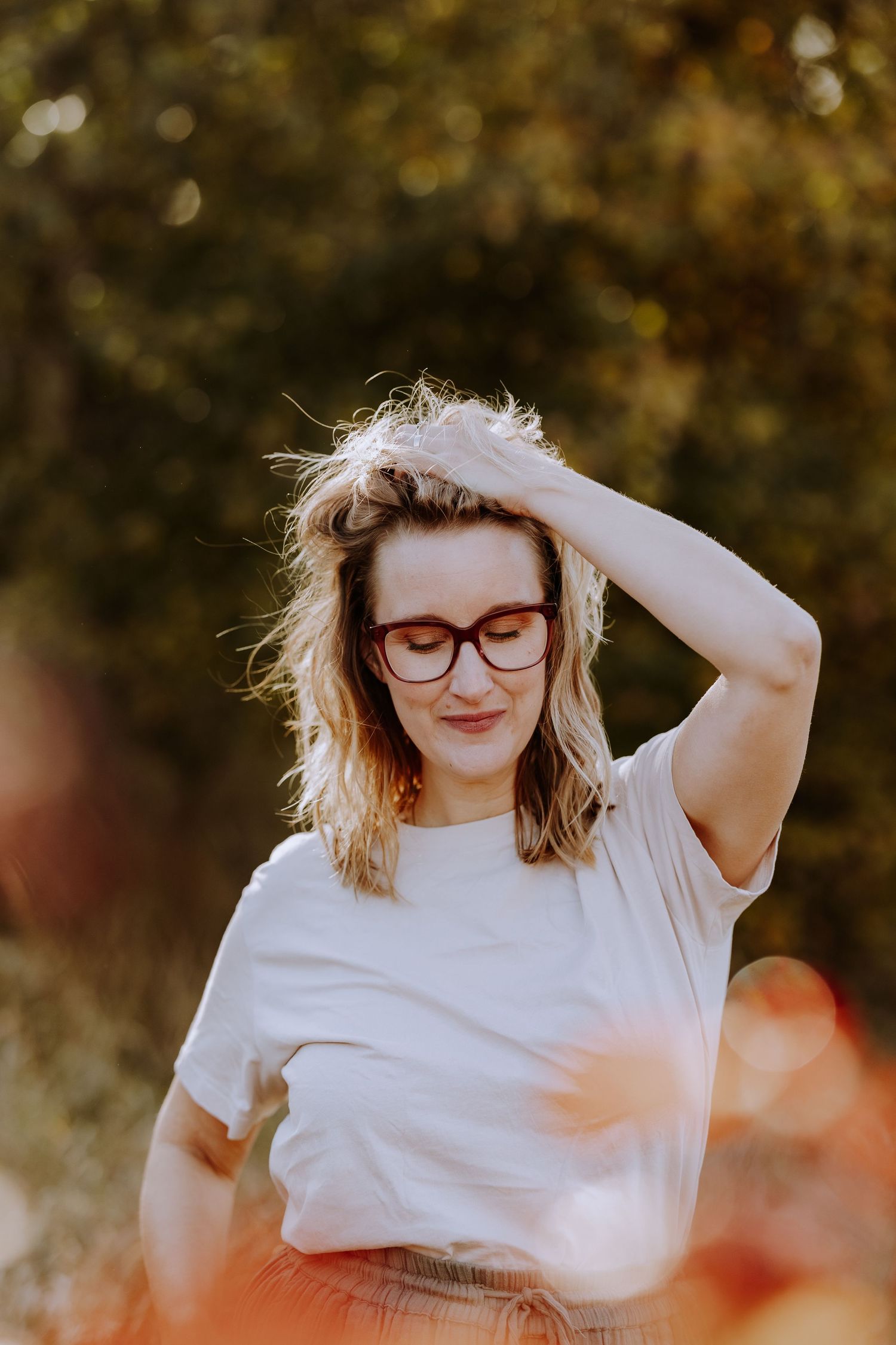 Close-up portrait with soft bokeh effect showing someone in glasses running fingers through hair.