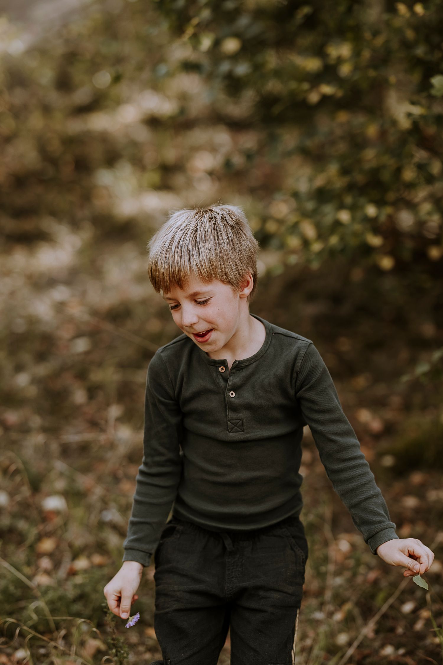 Young child in dark henley shirt smiling while playing outdoors in autumn.