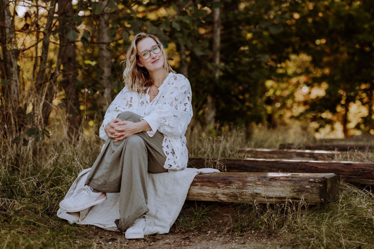 Someone in a white lacy top and pants sits casually on wooden steps outdoors.